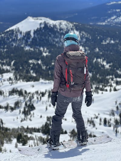 A snowboarder with a backpack prepares to snowboard down a hill.