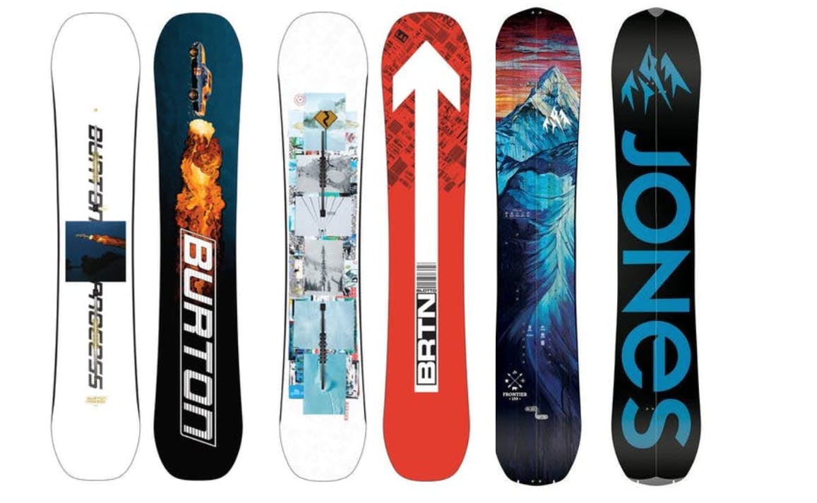 Three snowboards in a line with the bottom and top showing. From left to right, a white board, a blue board with fire on it, a white board with blue graphics, a red board with a white arrow, a blue board with a mountain scene, and a black board with a mountain and the word "JONES".