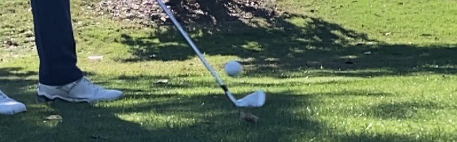 A golfer hits a ball with his iron.