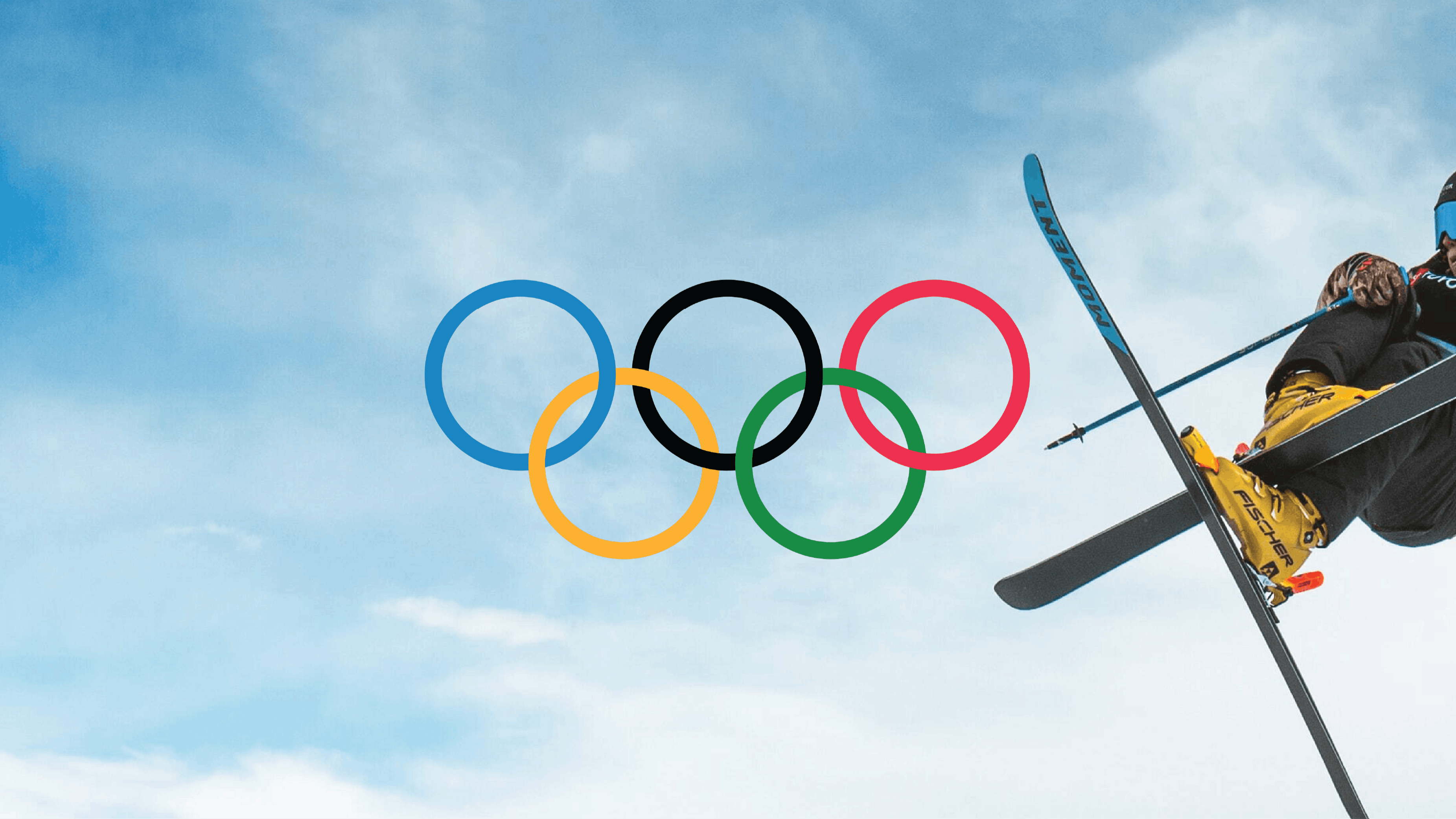 A skier jumps in the air and crosses his skis. The sky behind him is blue and dusted with clouds. The Olympic rings are added on top.
