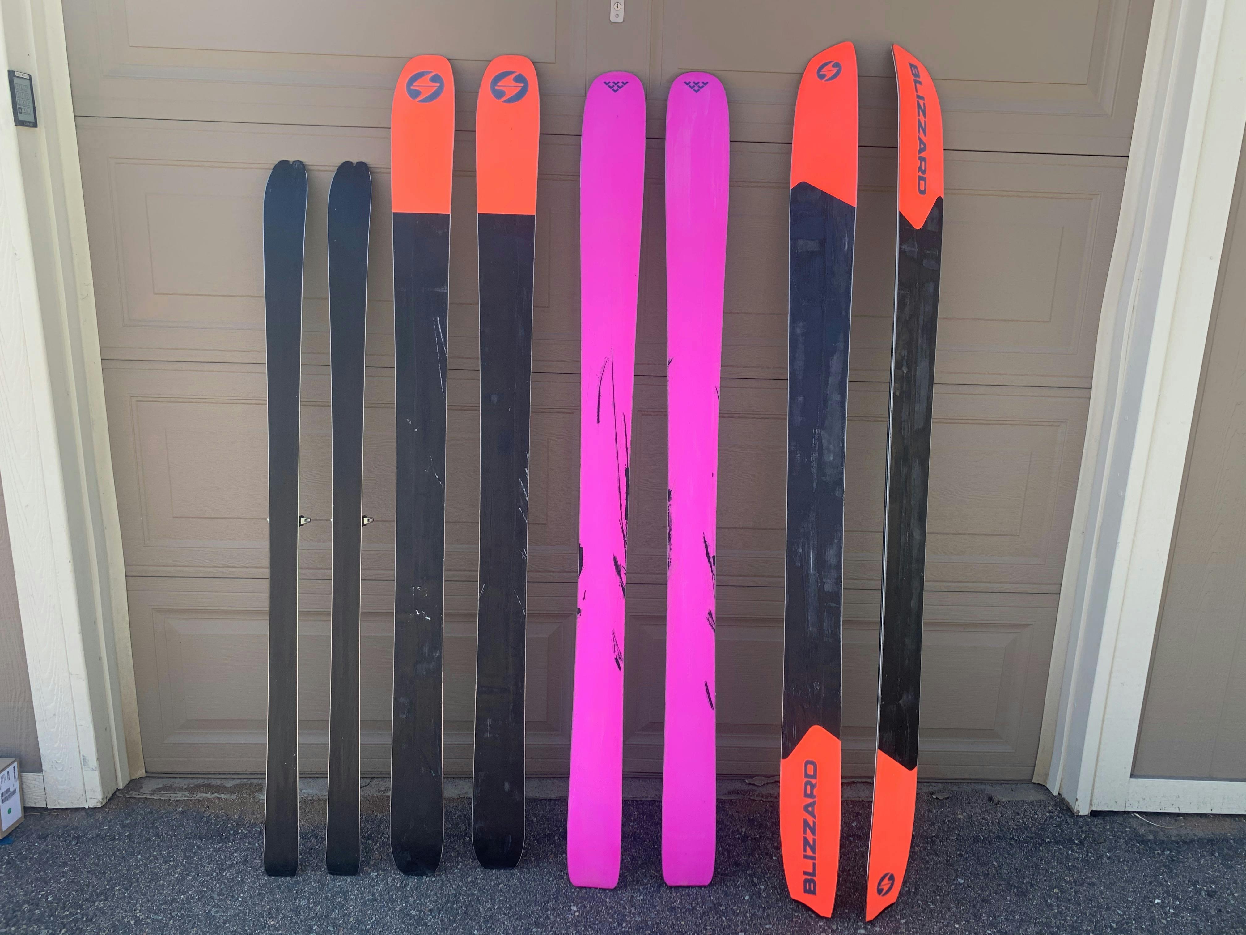 Four pairs of used skis leaning against a garage door