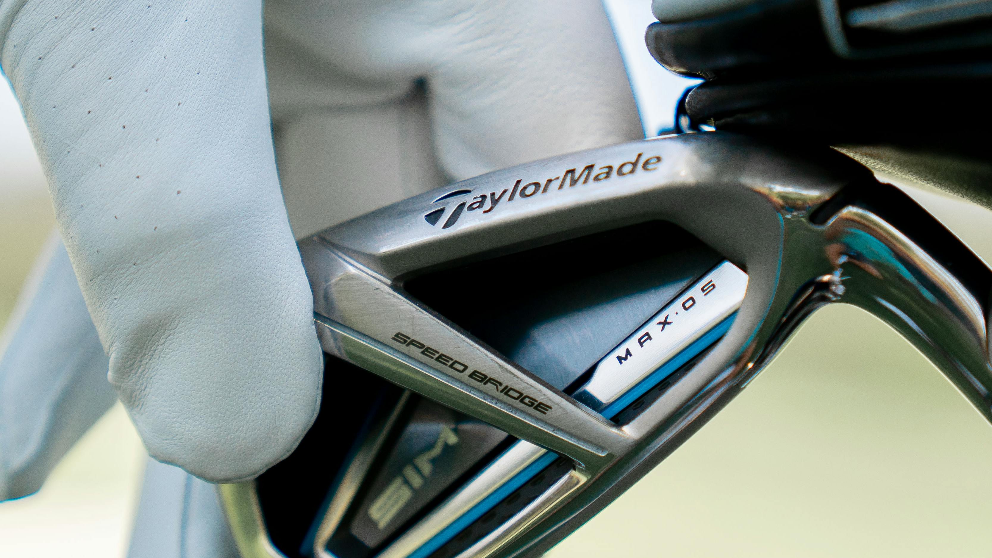 Someone in a white golf glove pulls a TaylorMade iron out of a golf bag.