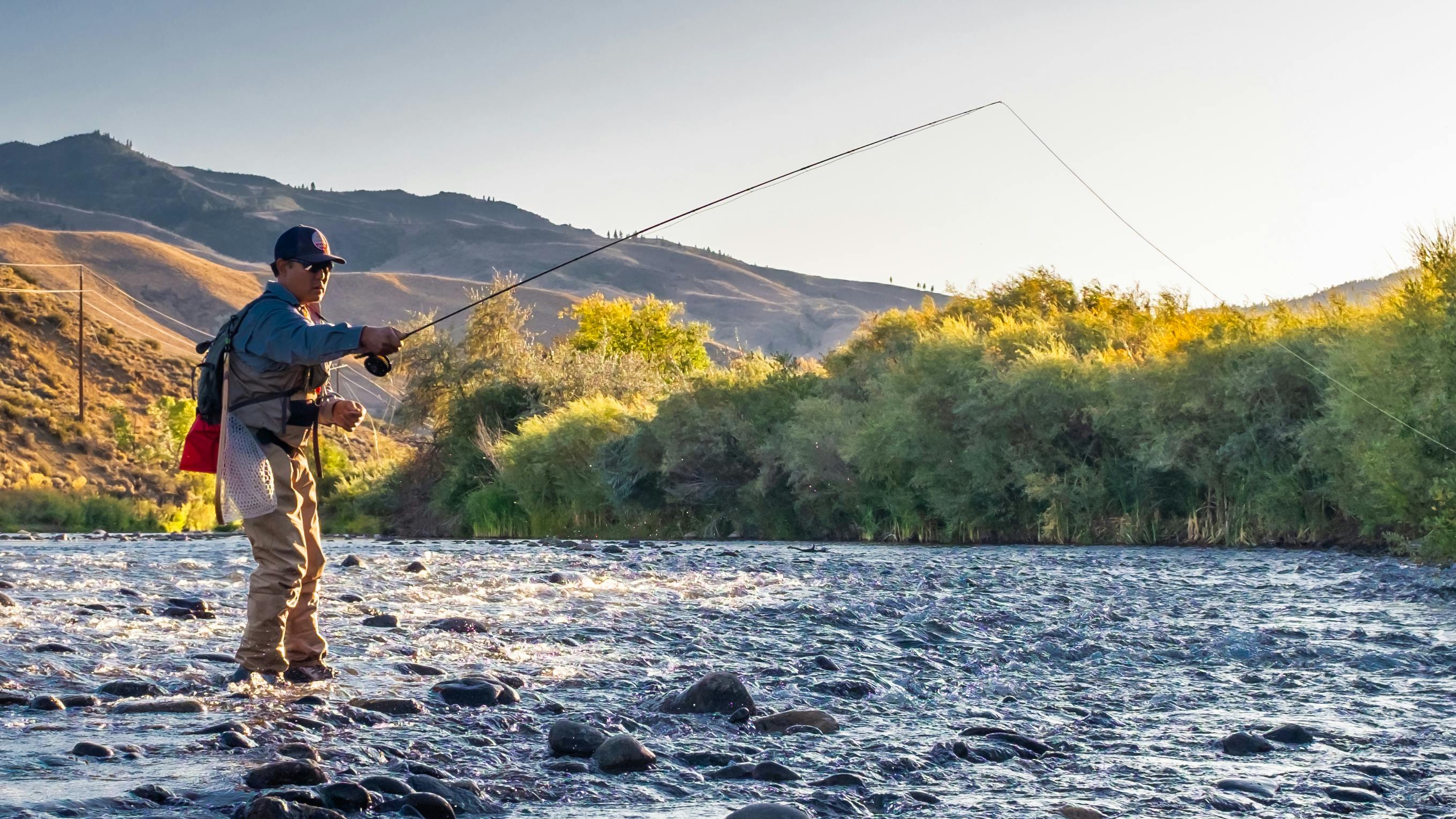 A man casts a fly fishing rod while standing in a river
