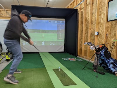 A man takes a swing with a driver in a golf simulator.