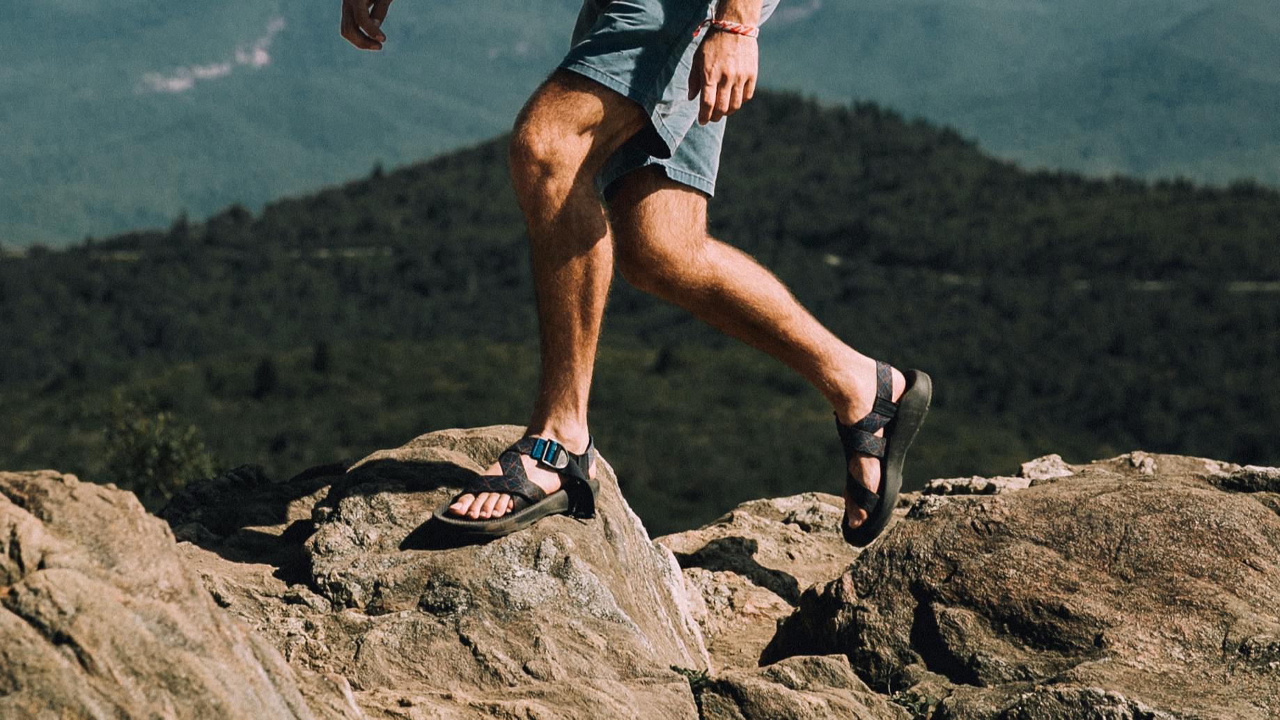 A man in sandals hikes on a rocky ridgeline.