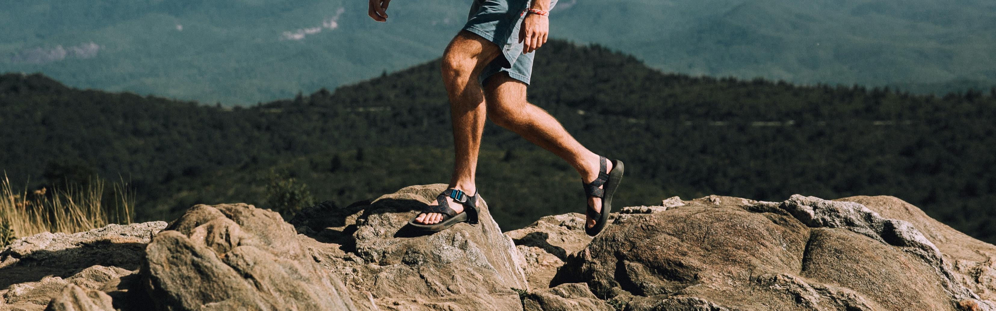 A man in sandals hikes on a rocky ridgeline.