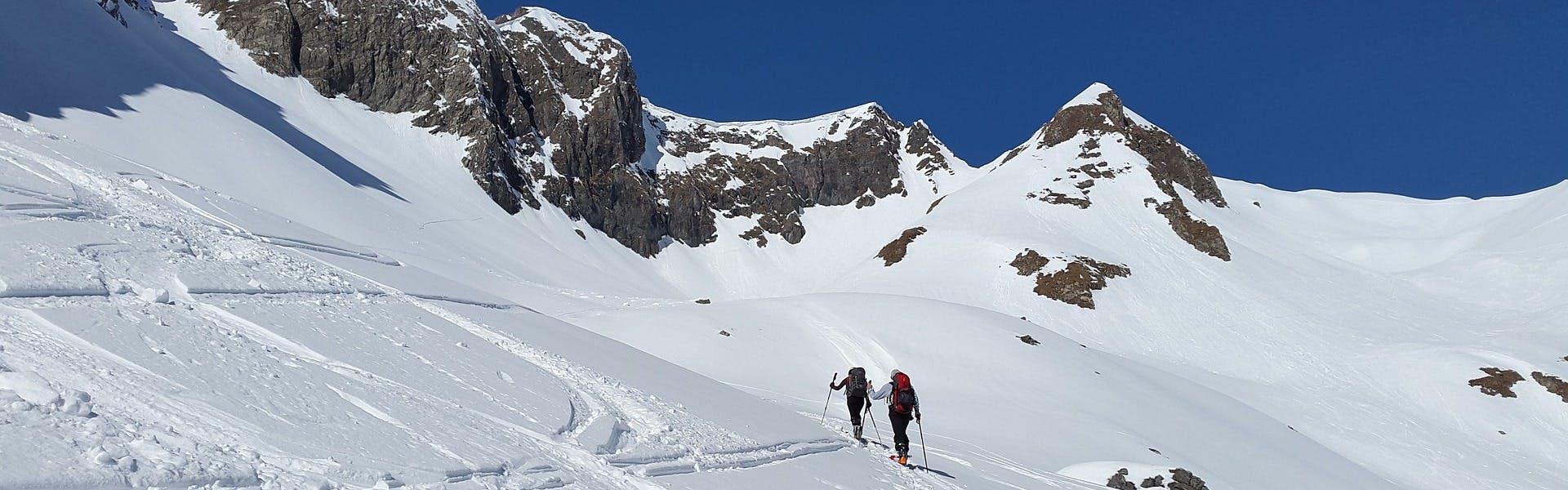 Two people backcountry ski uphill.
