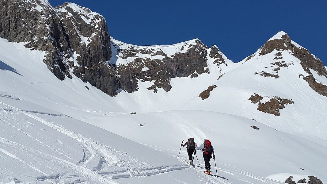 Two people backcountry ski uphill.