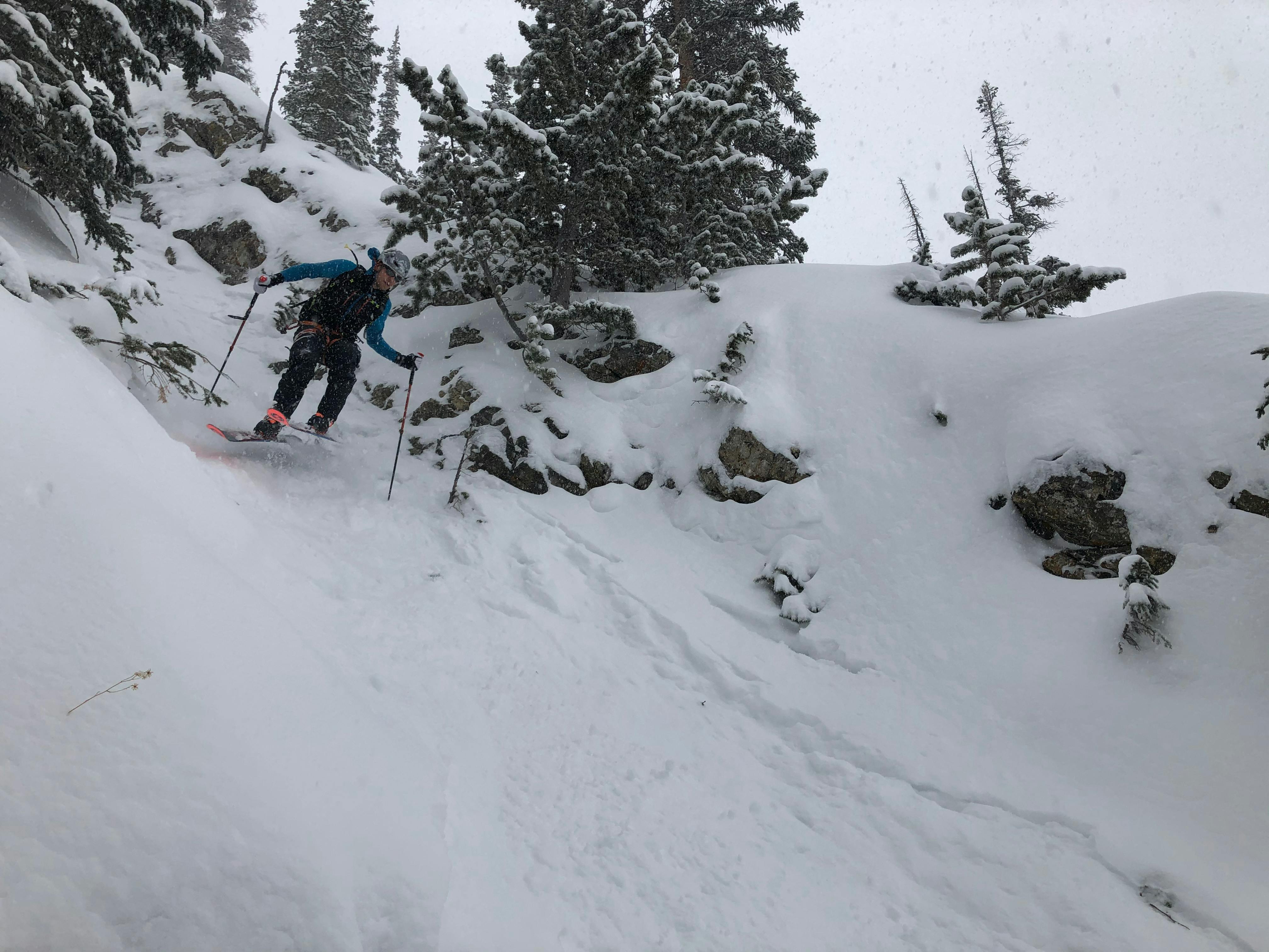 A skier heading down a steep slope in the backcountry on a cloudy day