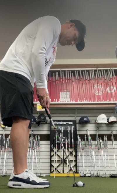 A man in a golf store using the  Odyssey DFX 2-Ball Putter.