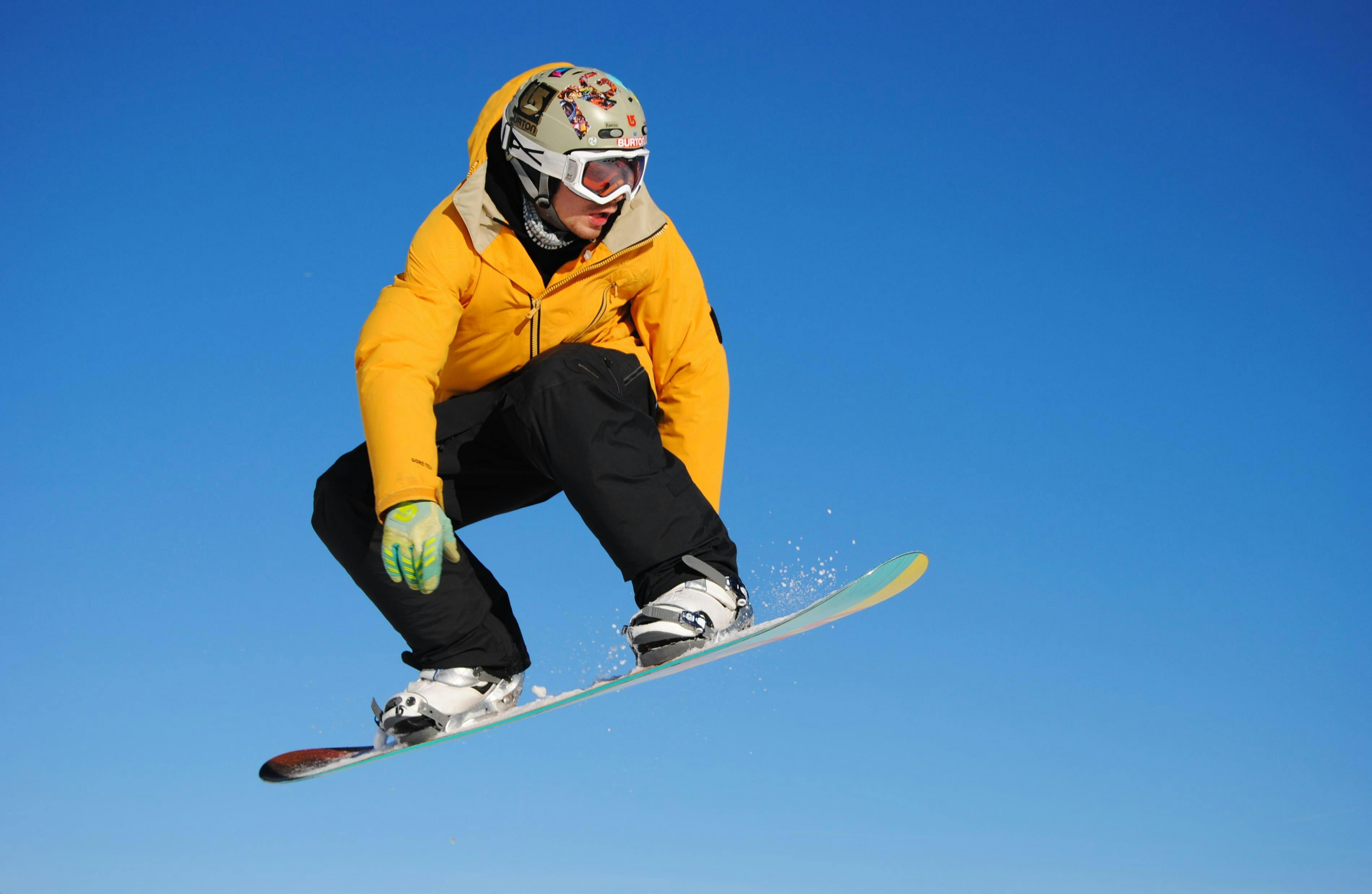 A snowboarder jumps on their board on a blue-sky day. 