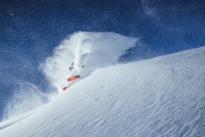 A skier sending out a wave of powder while turning on a steep snowy slope
