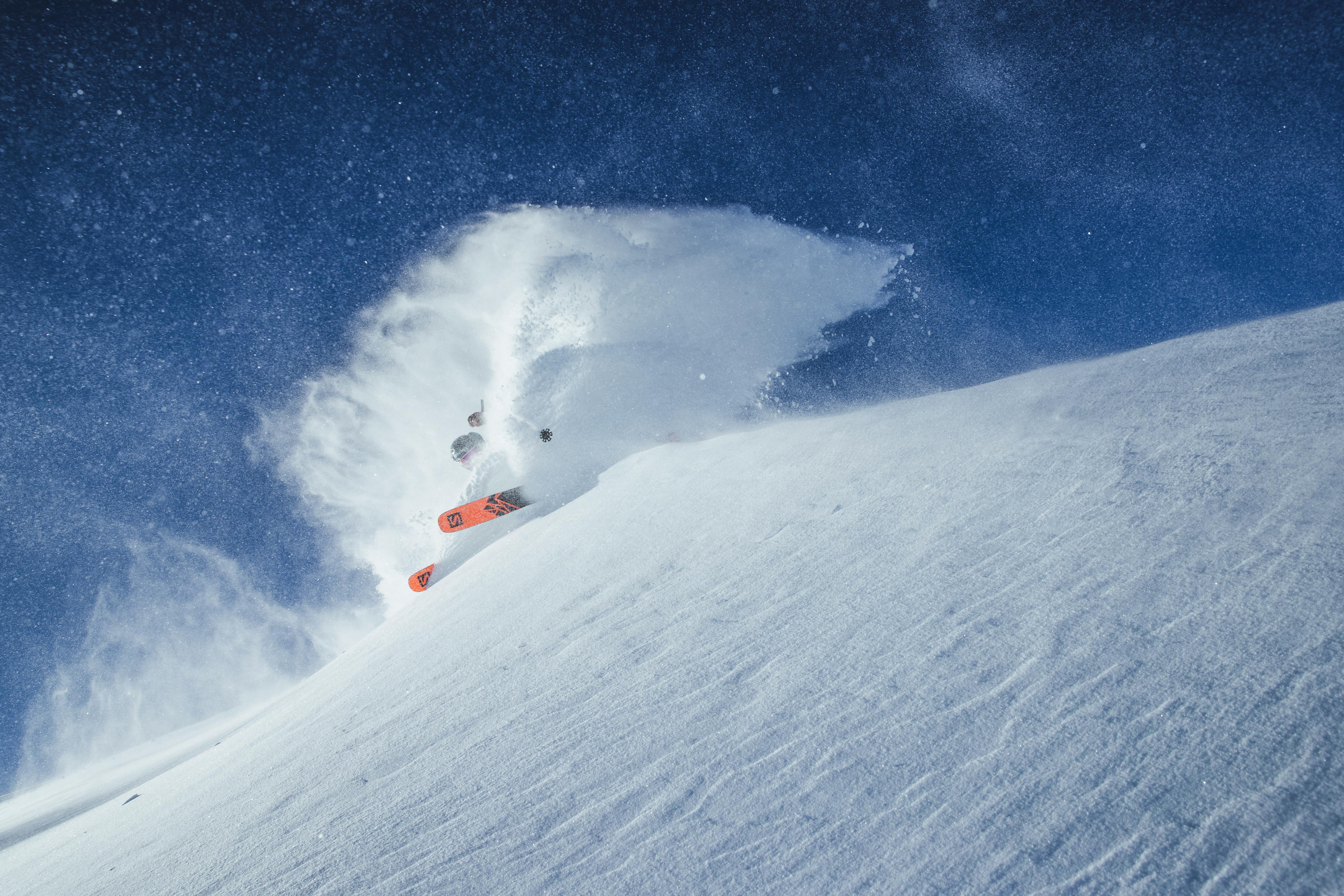 A skier sending out a wave of powder while turning on a steep snowy slope