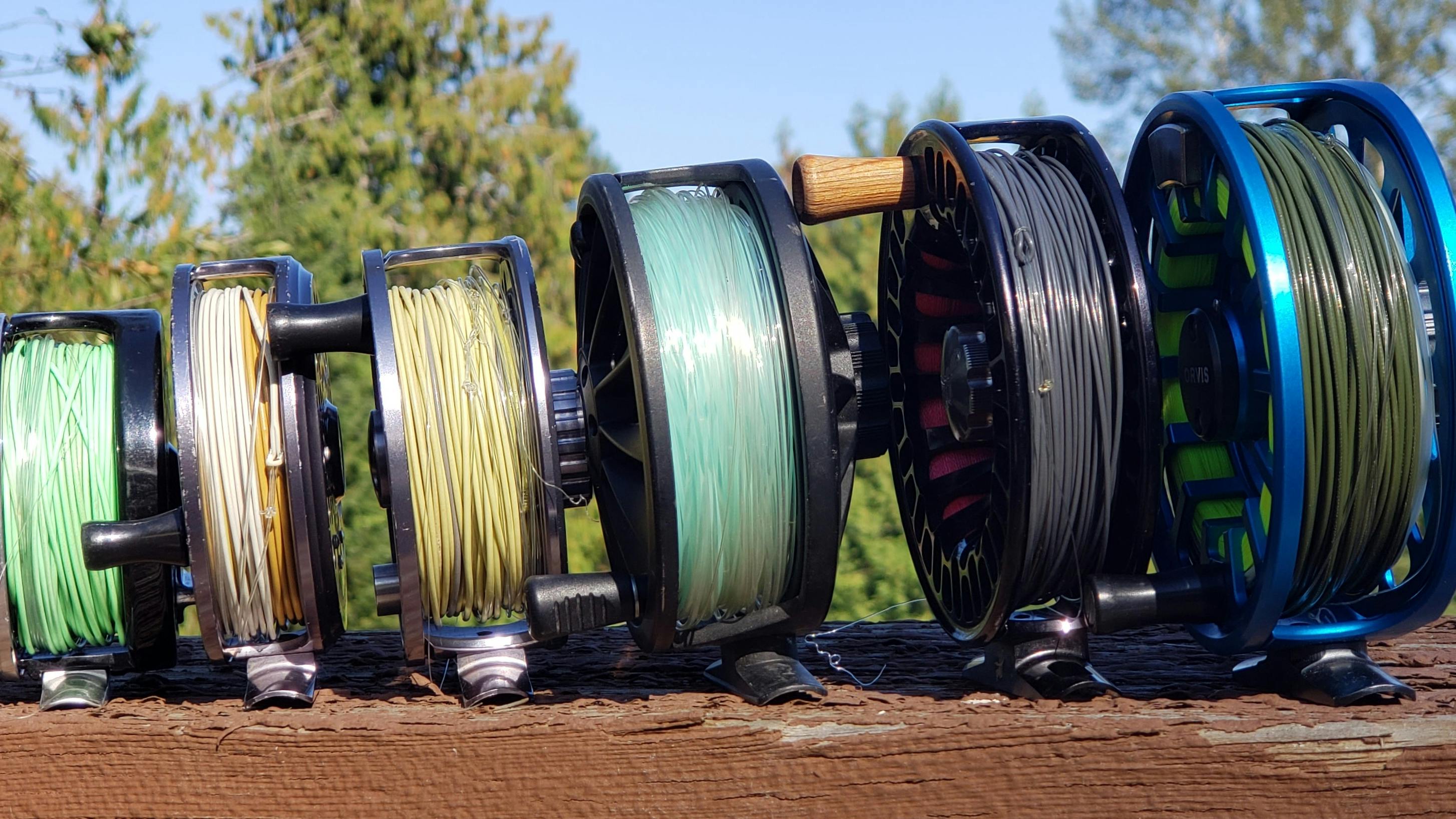 Six different fly fishing reels sitting in a line. 