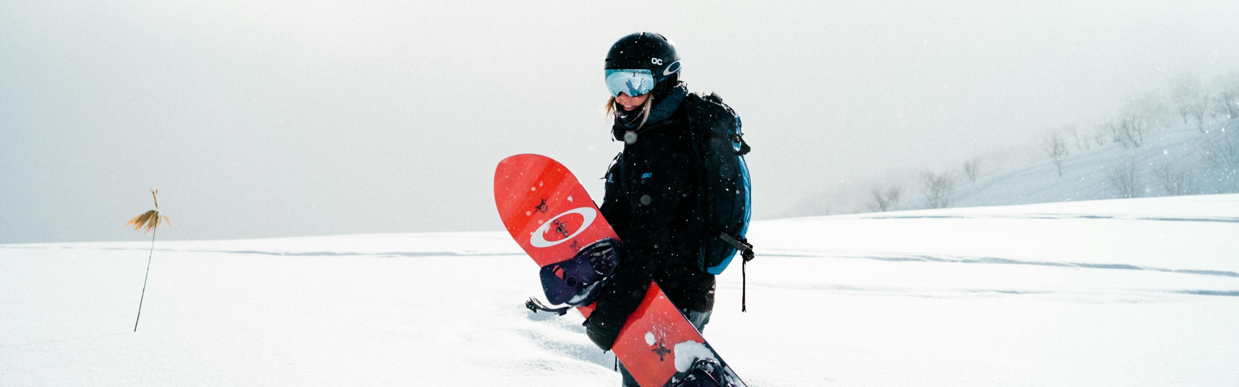 A woman holding a snowboard and smiling at the camera. 