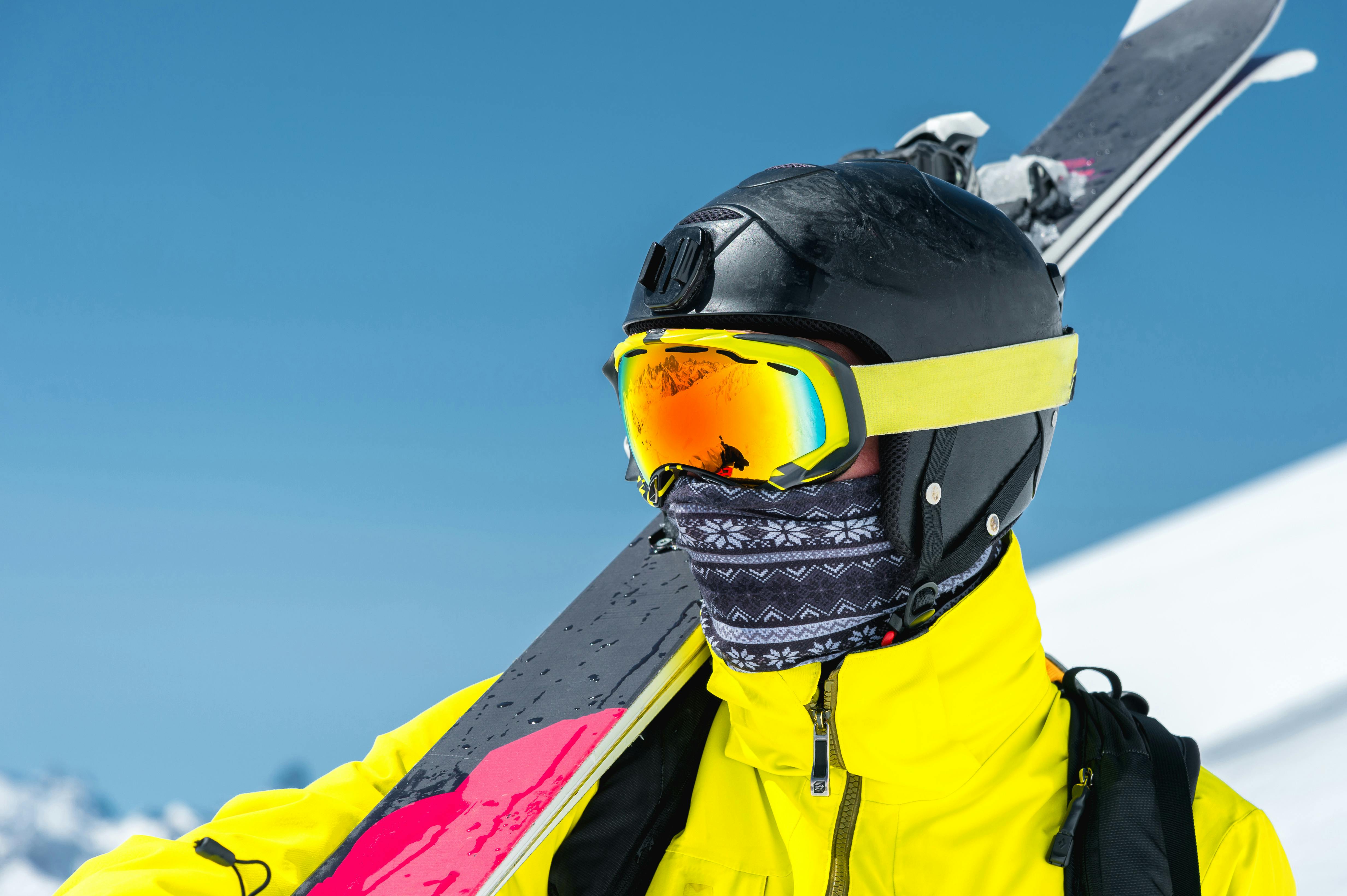 A skier in a face covering holds their skis over their shoulder