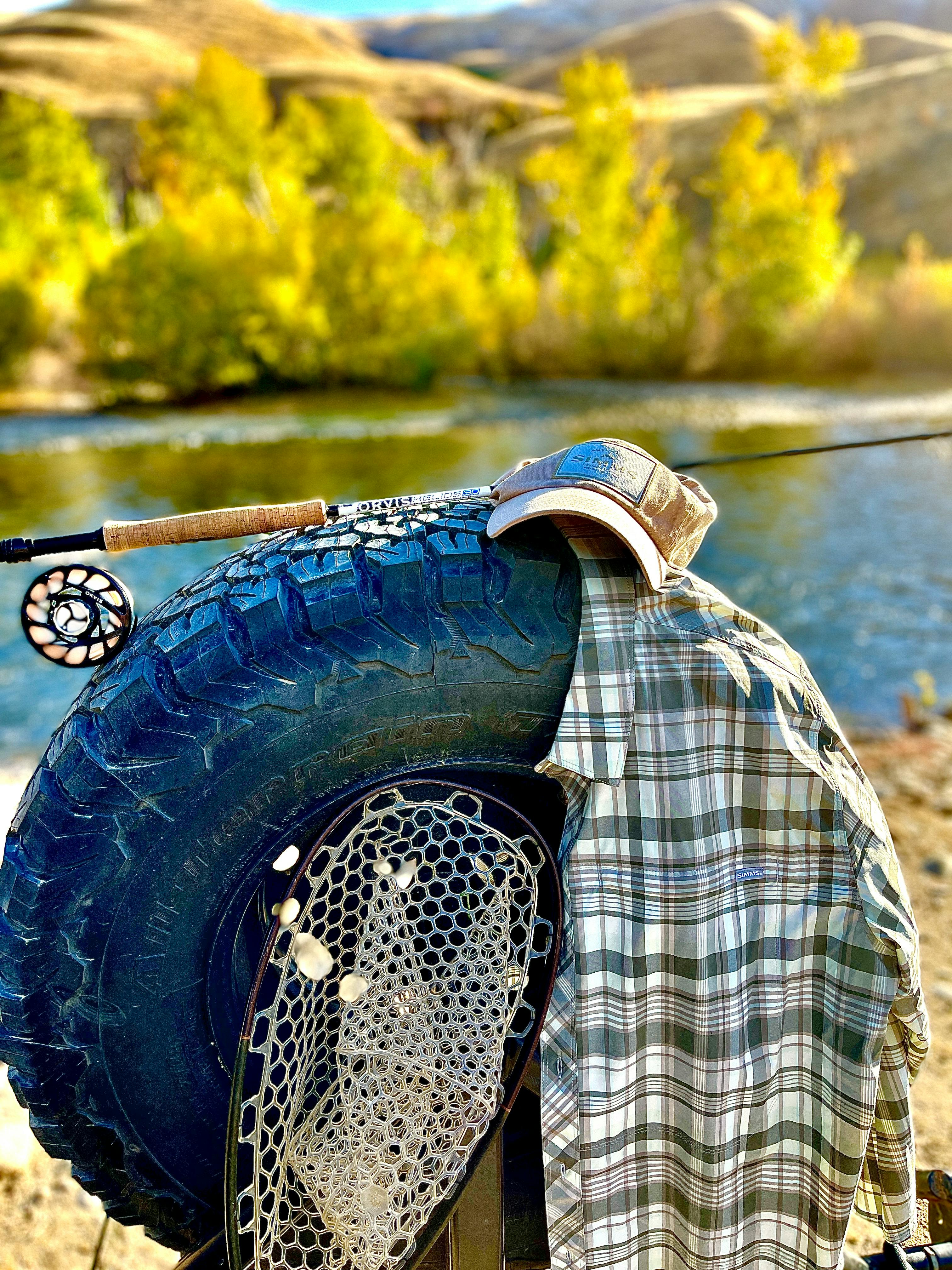 The Simms Stone Cold Shirt hanging on a tire with a fly rod and net next to it. 