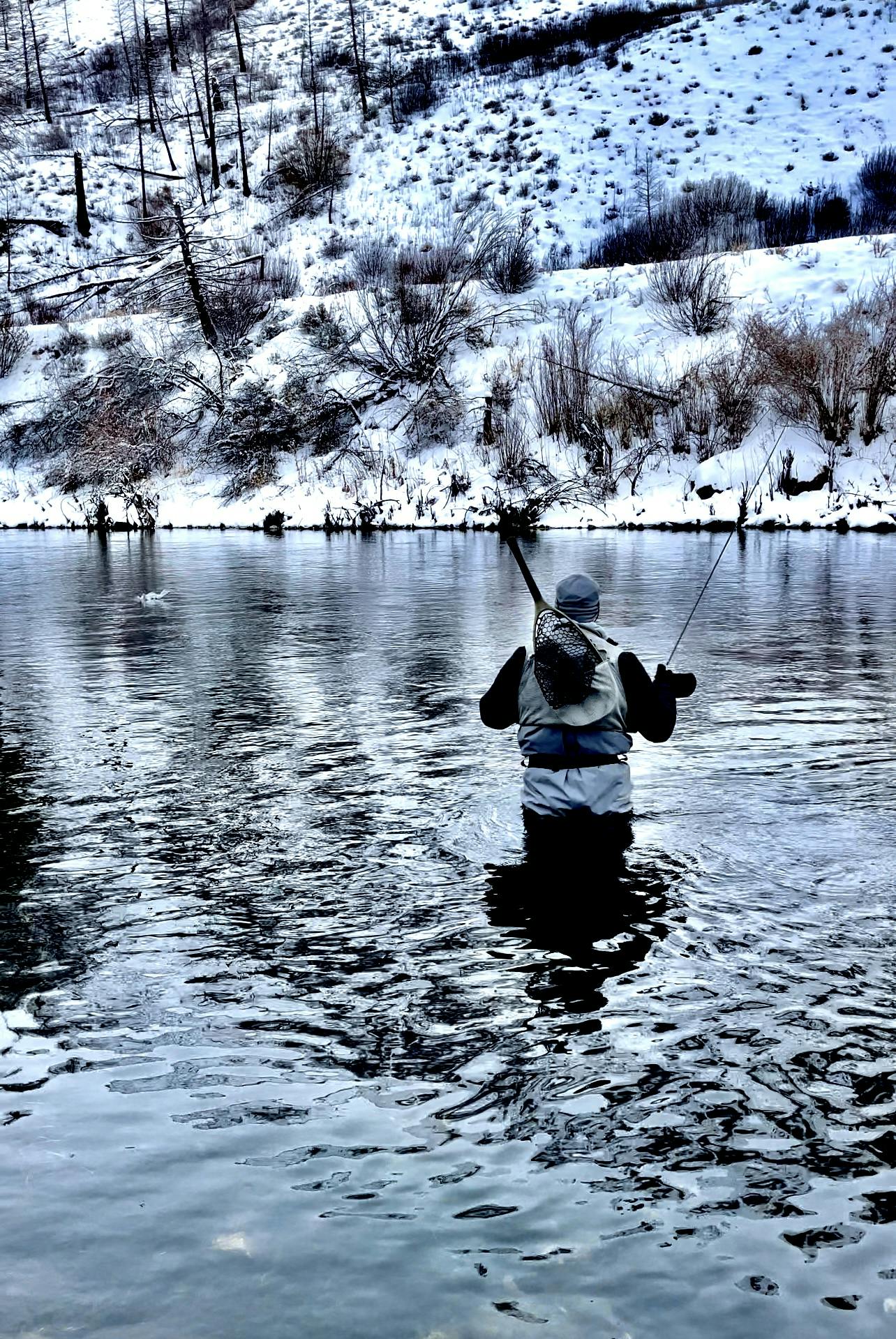 A fisherman standing in a river with snow all around him. 