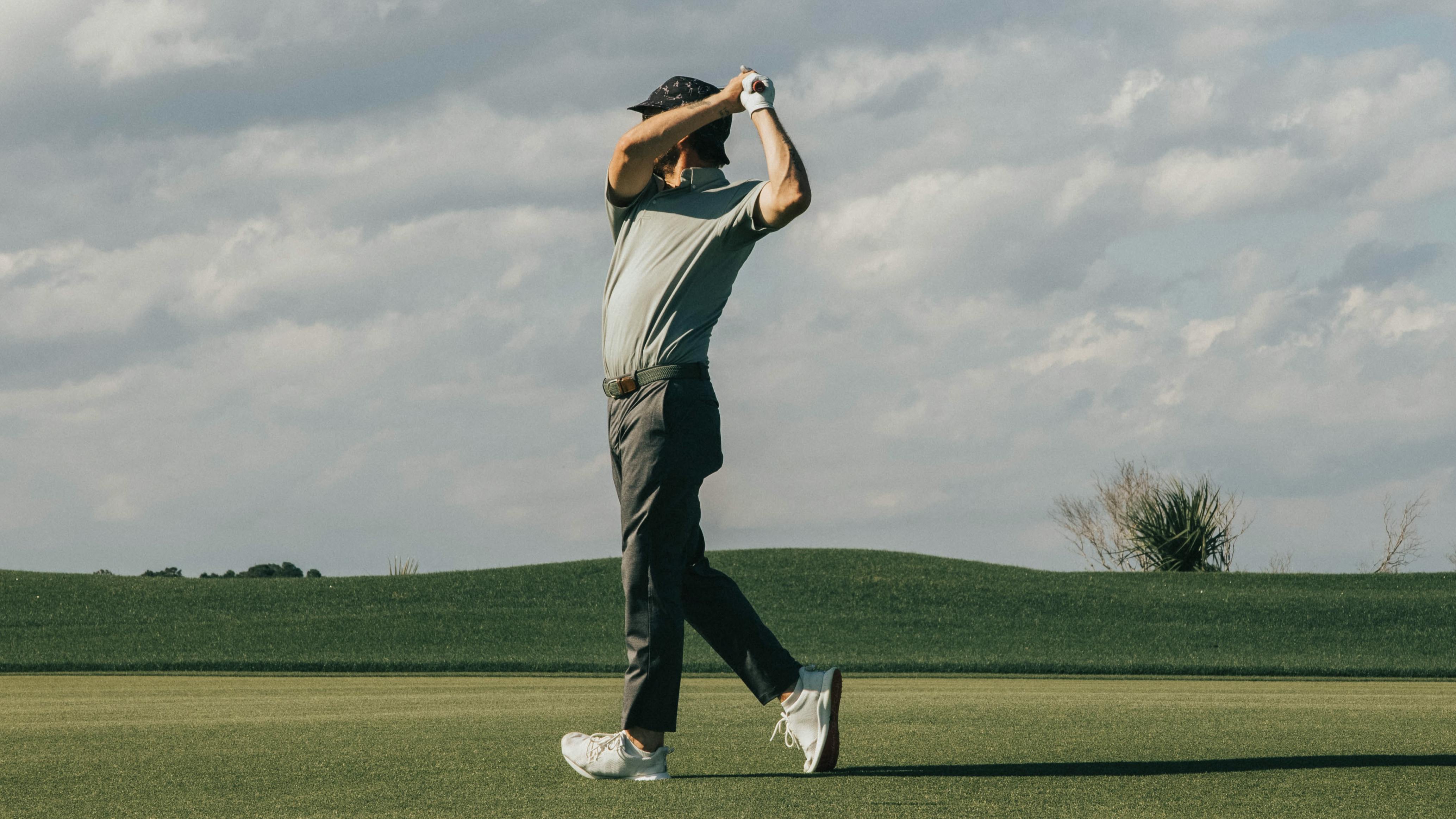 A man stands perpendicular to the camera and swings his golf club back, his arms obscuring his face.
