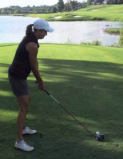 A woman swinging a driver on a golf course.