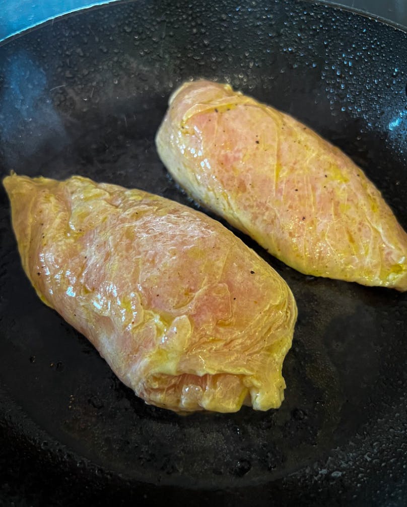 Two chicken breasts face down in a pan. 