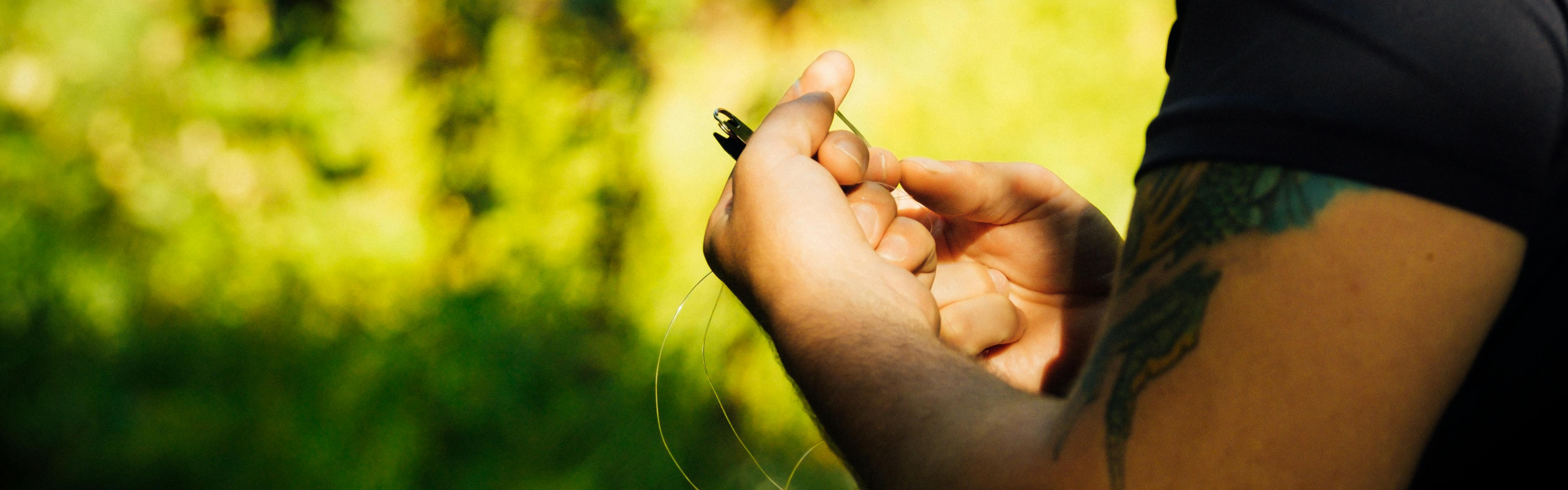 A man holds fishing line in his hands against a green background of foliage. 