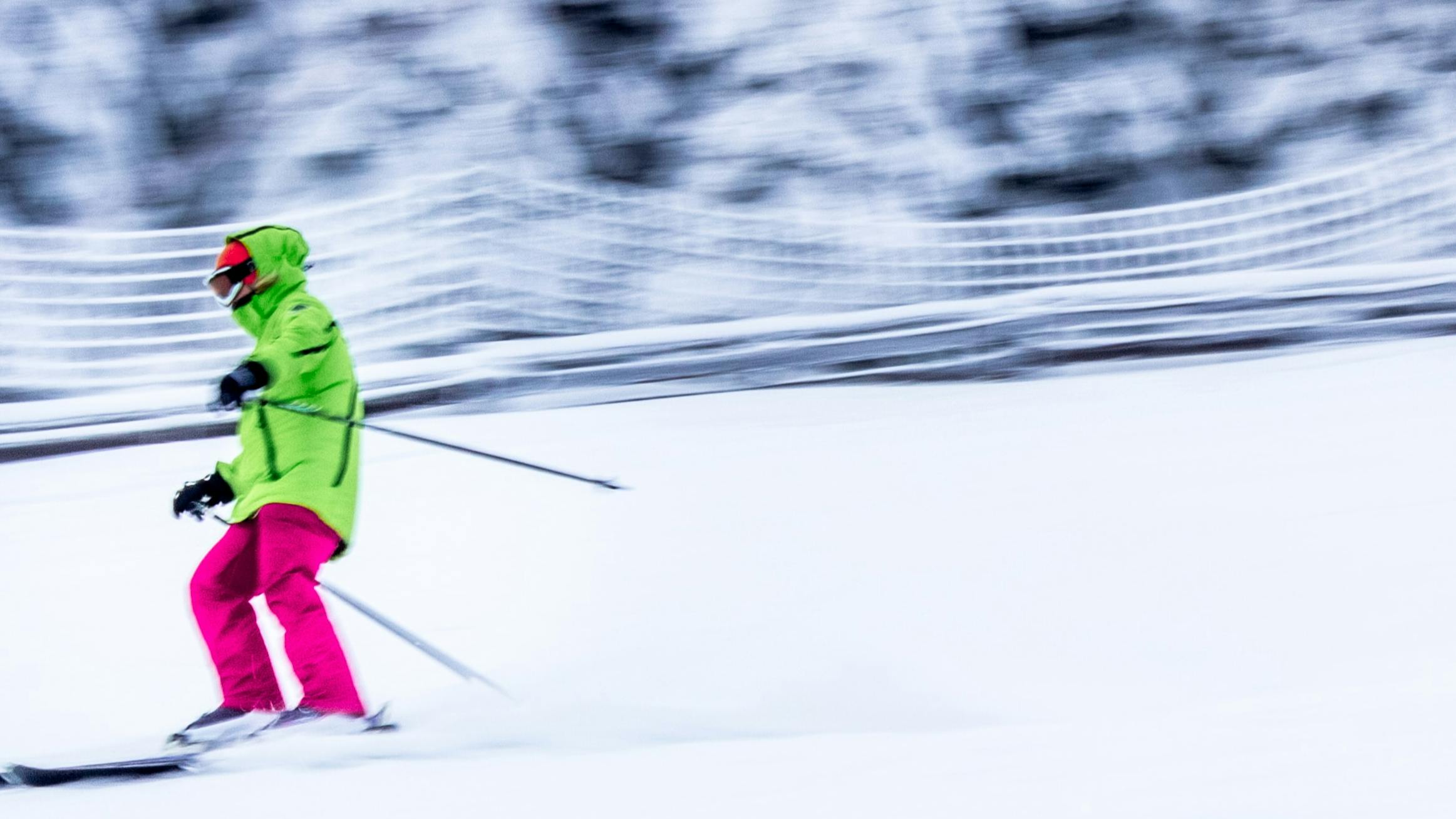 Skier zooming down the frosty white slope in a neon green jacket and hot pink ski pants.