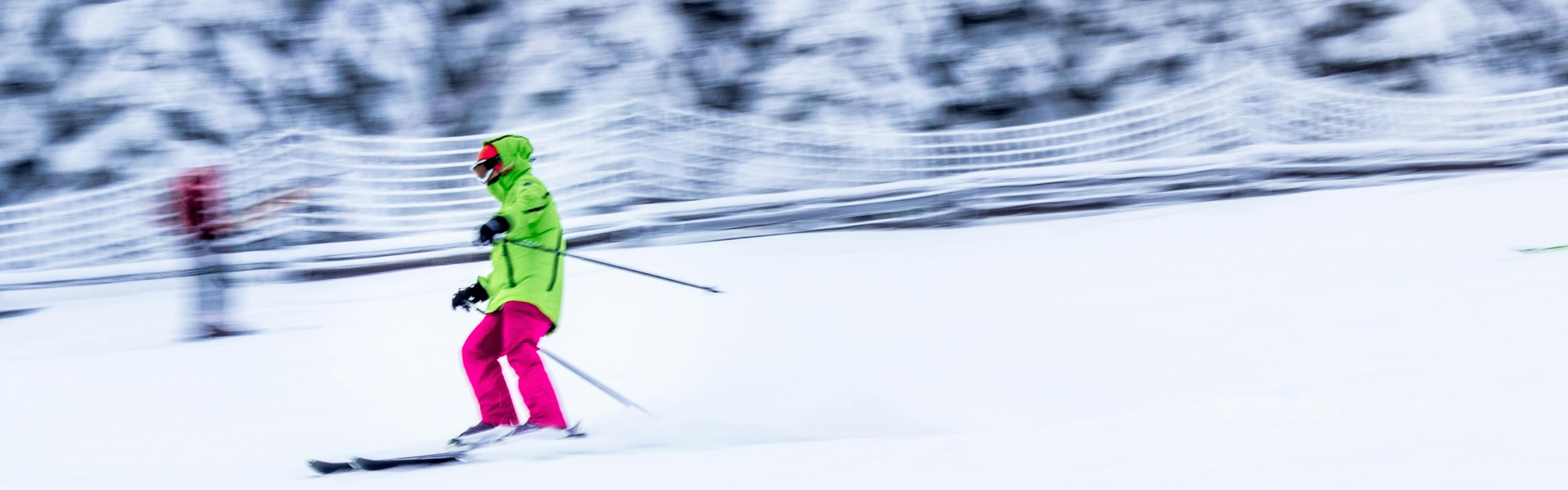 Skier zooming down the frosty white slope in a neon green jacket and hot pink ski pants.