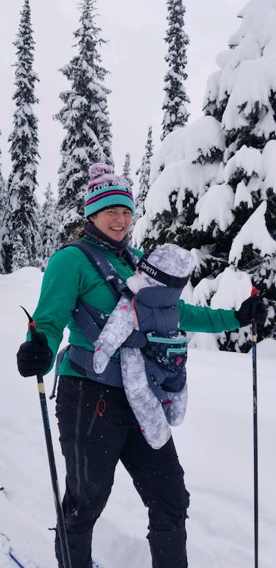 A mom nordic skiing while holding a baby in a baby carrier. 