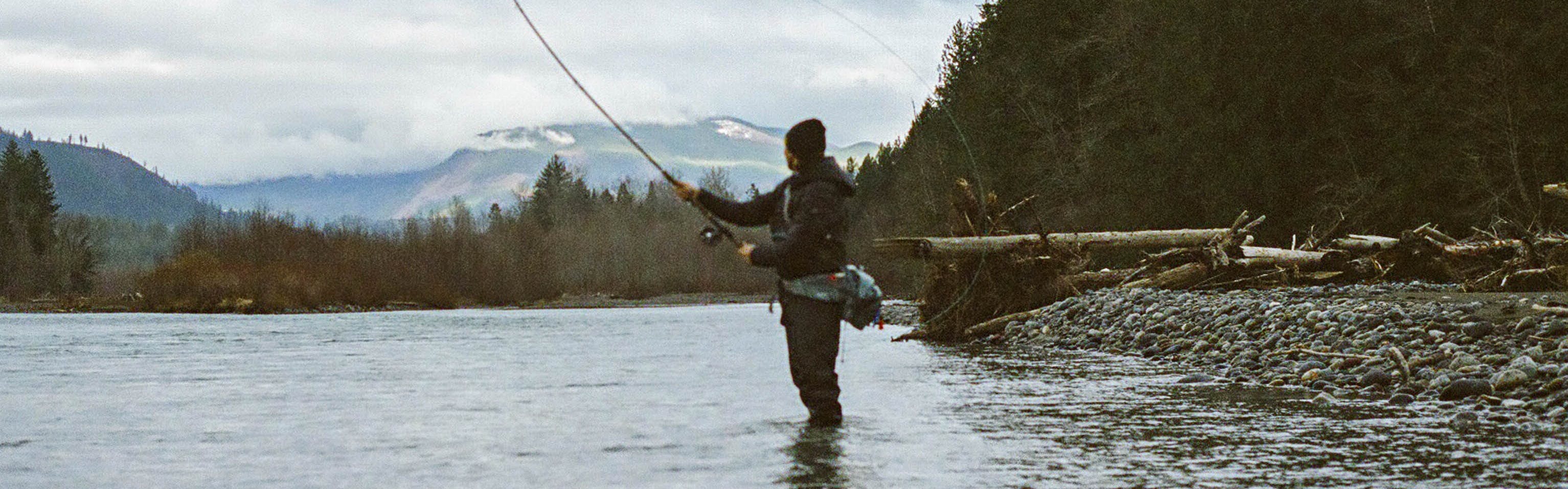 A man stands in the water casting a fly fishing rod