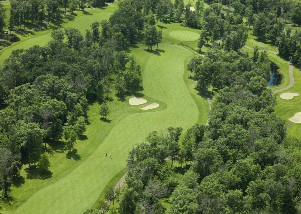 An aerial view of a vibrantly green golf course with trees and sand bunkers