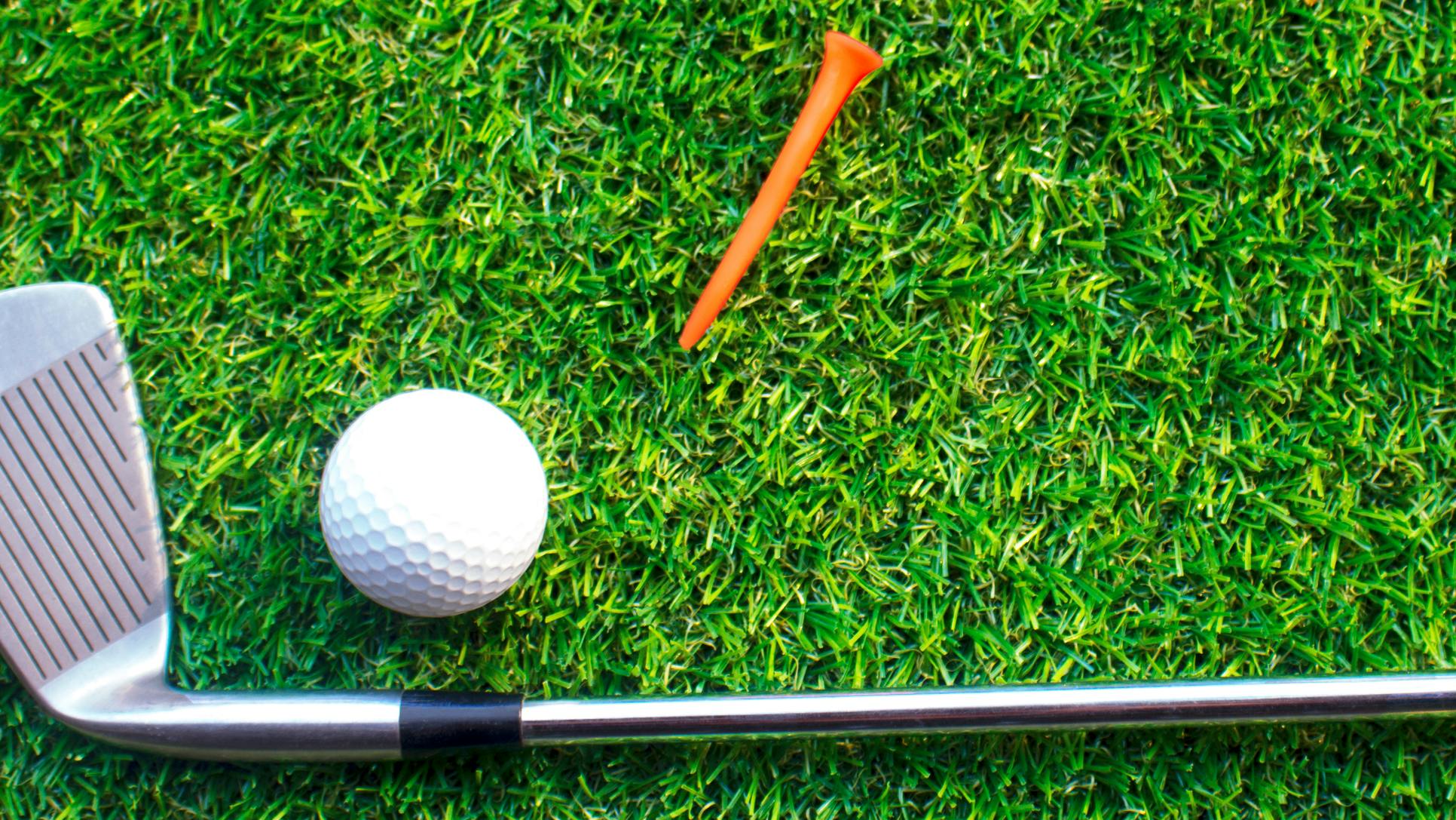 A golf club rests on the grass next to a golf ball and an orange tee