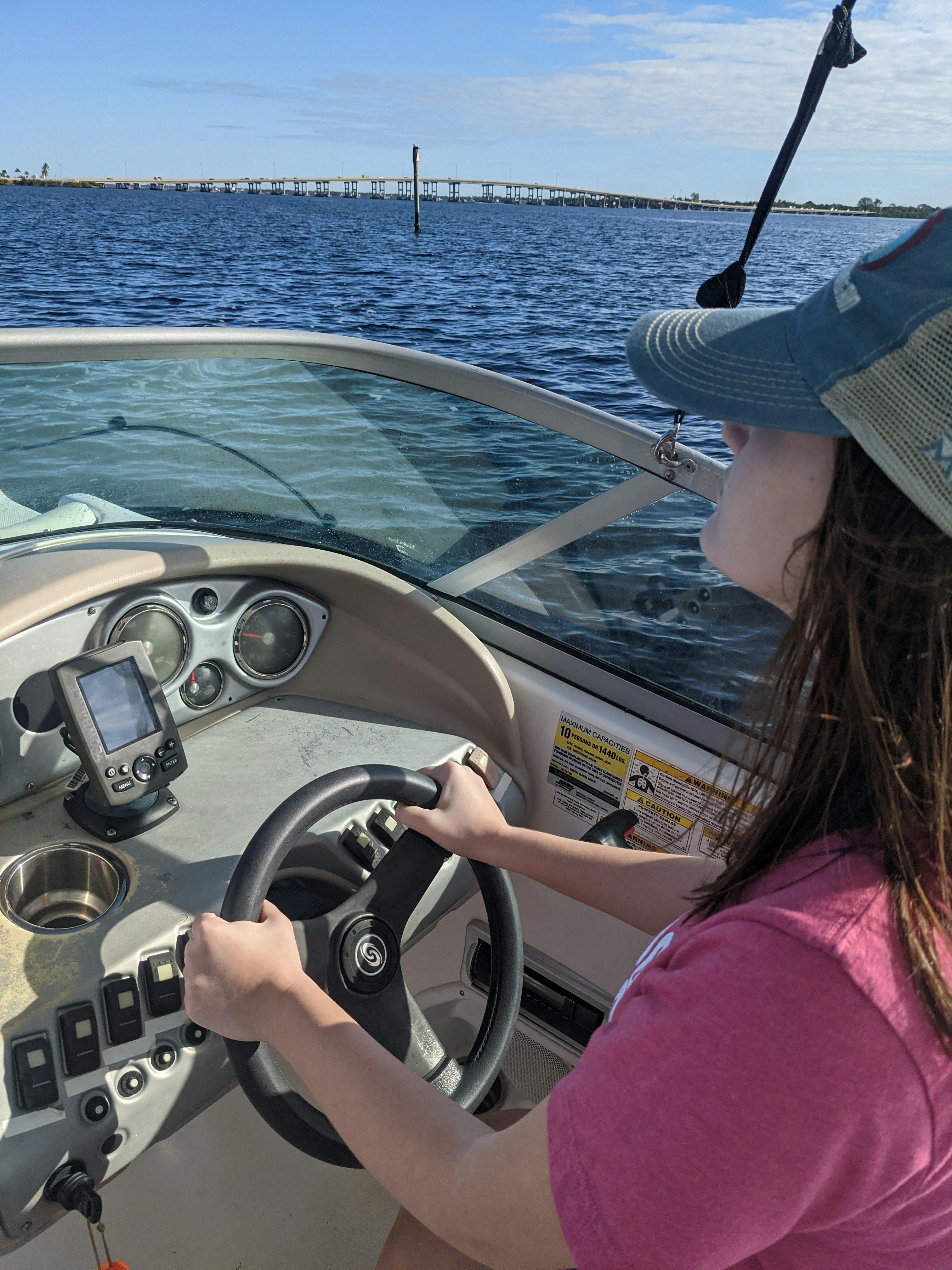 A woman sits at the wheel of a boat and steers. 