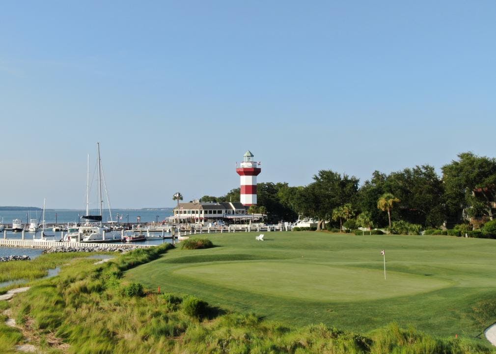 A golf course by a marina and a red and white striped lighthouse