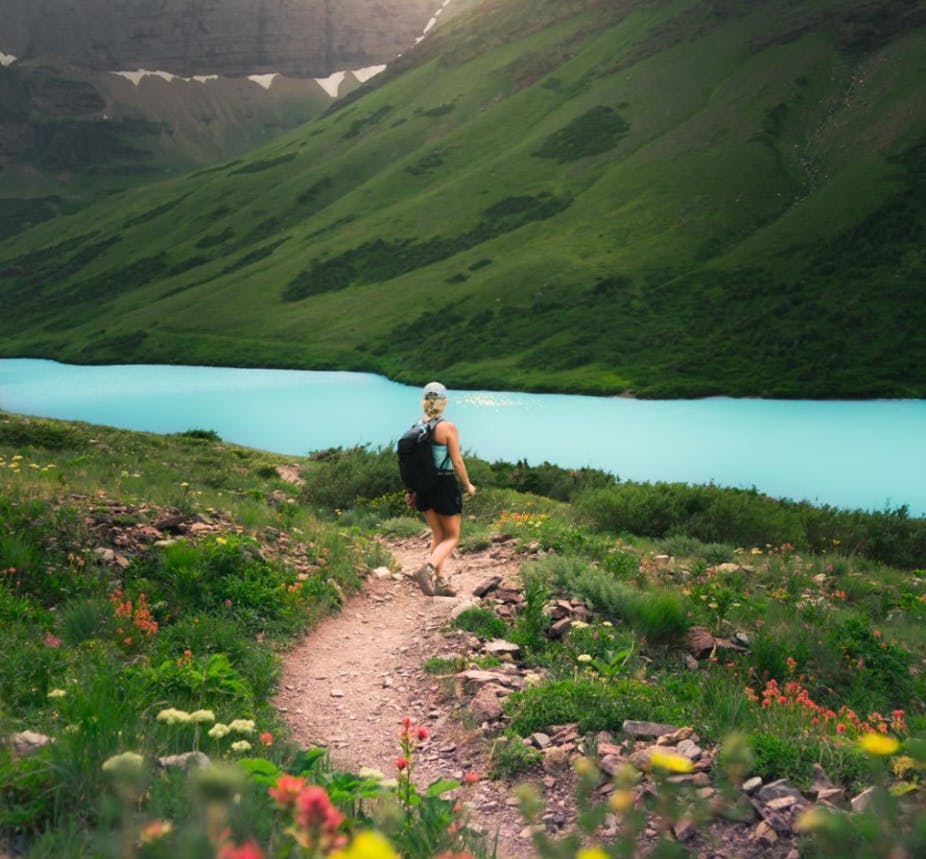 A woman hiking on a trail towards a lake. 