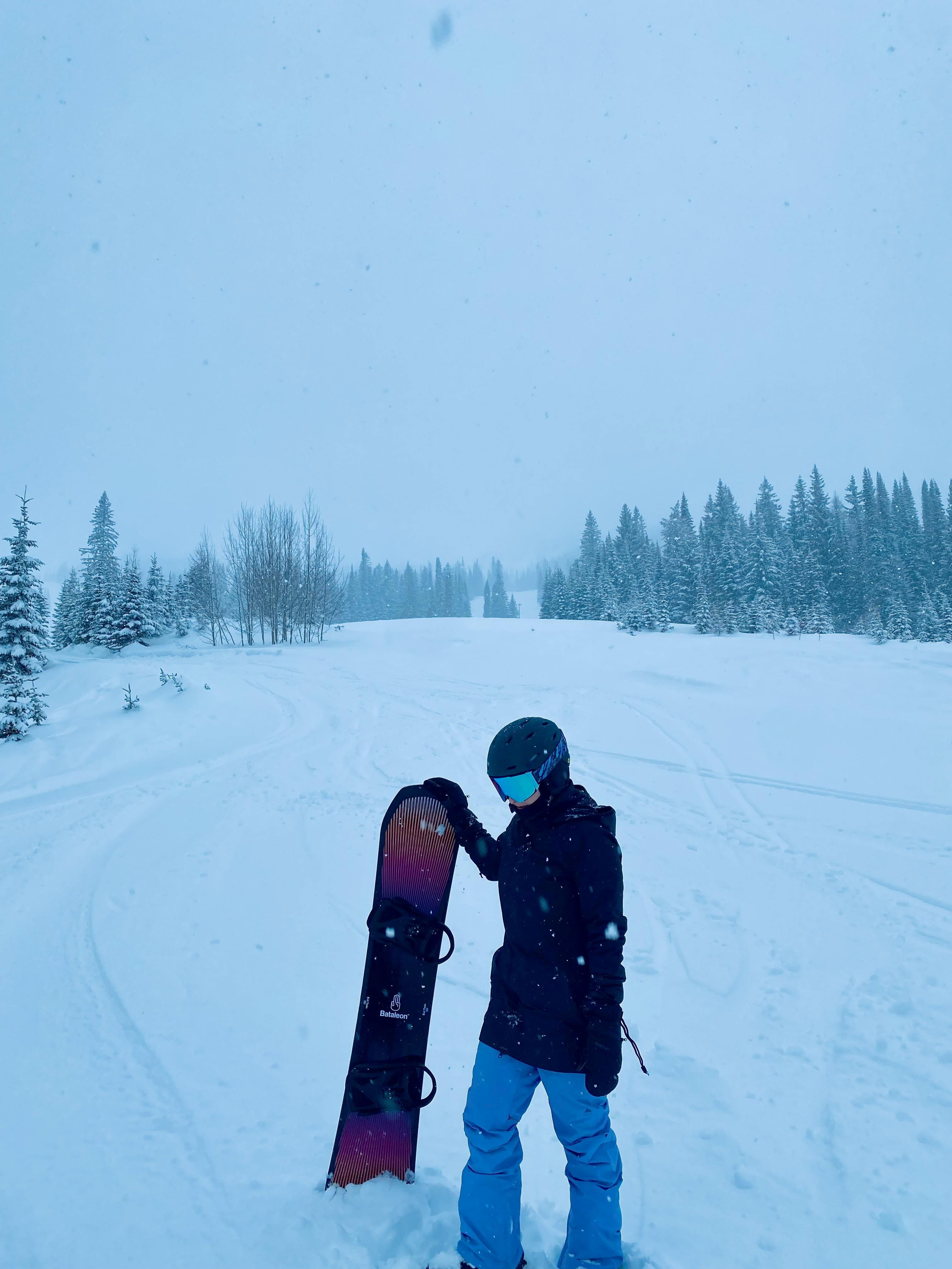 A woman stands with a snowboard at the bottom of a snowboard run. She is wearing the Burton Women's GORE-TEX® Avalon Bib Pants.