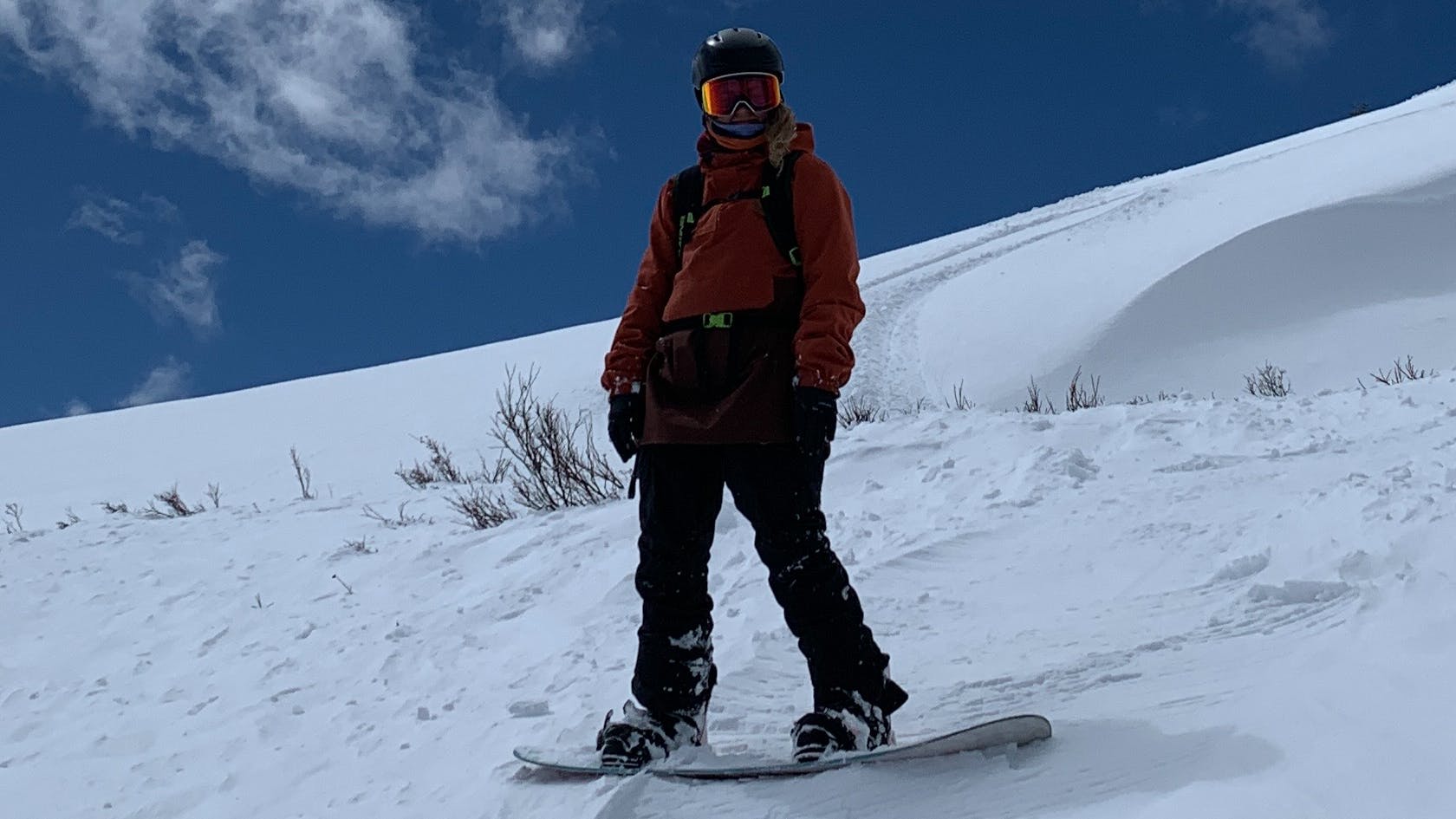 A woman on a snowboard stands perpendicular to the snowy slope she's on. The sky behind her is a dark blue.