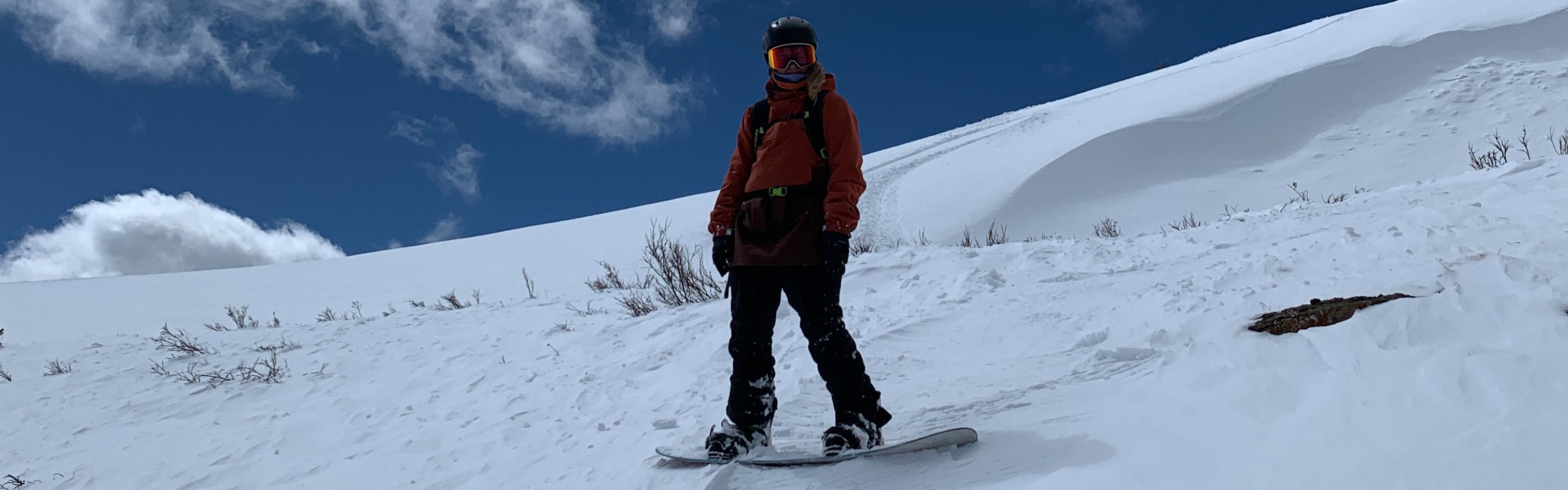 A woman on a snowboard stands perpendicular to the snowy slope she's on. The sky behind her is a dark blue.