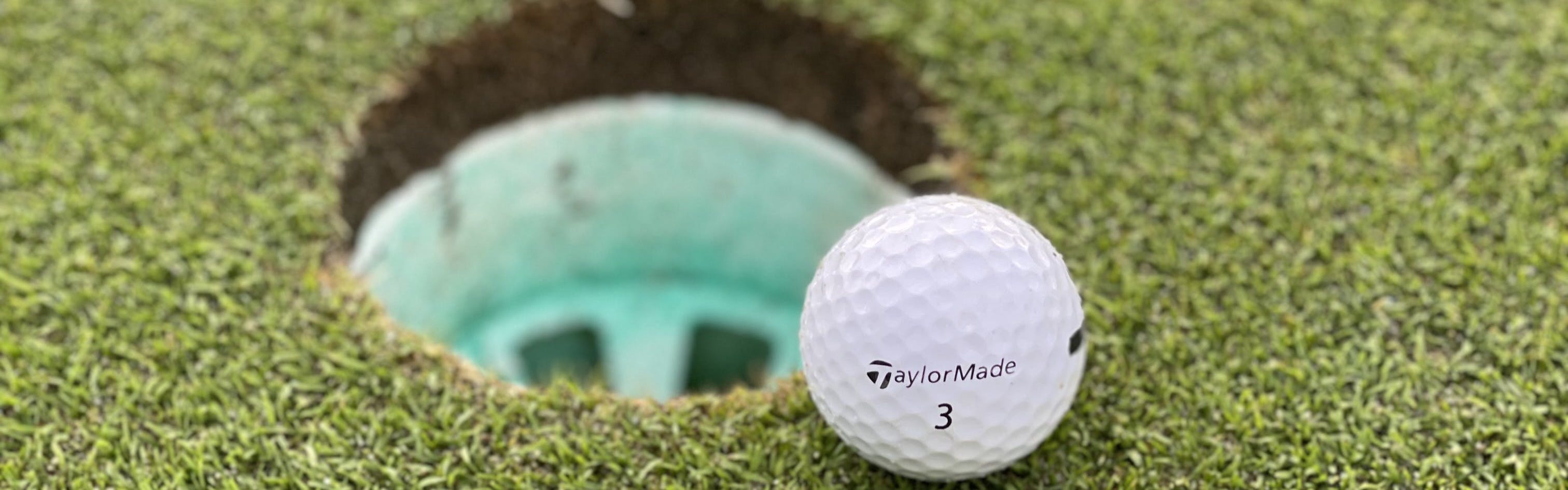 The TaylorMade Distance+ Golf ball in front of a hole.