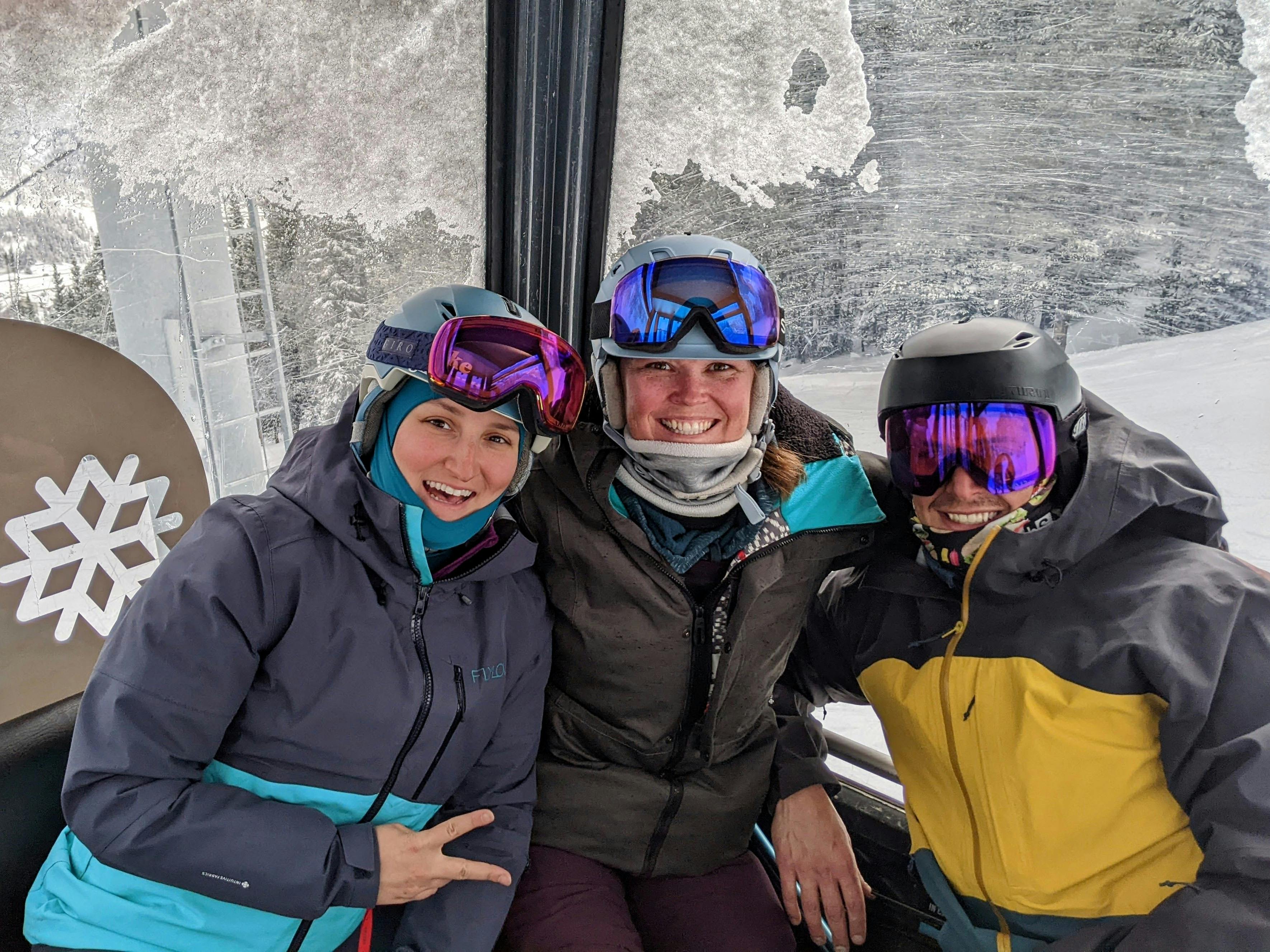Three people in ski gear sitting inside a gondola. 