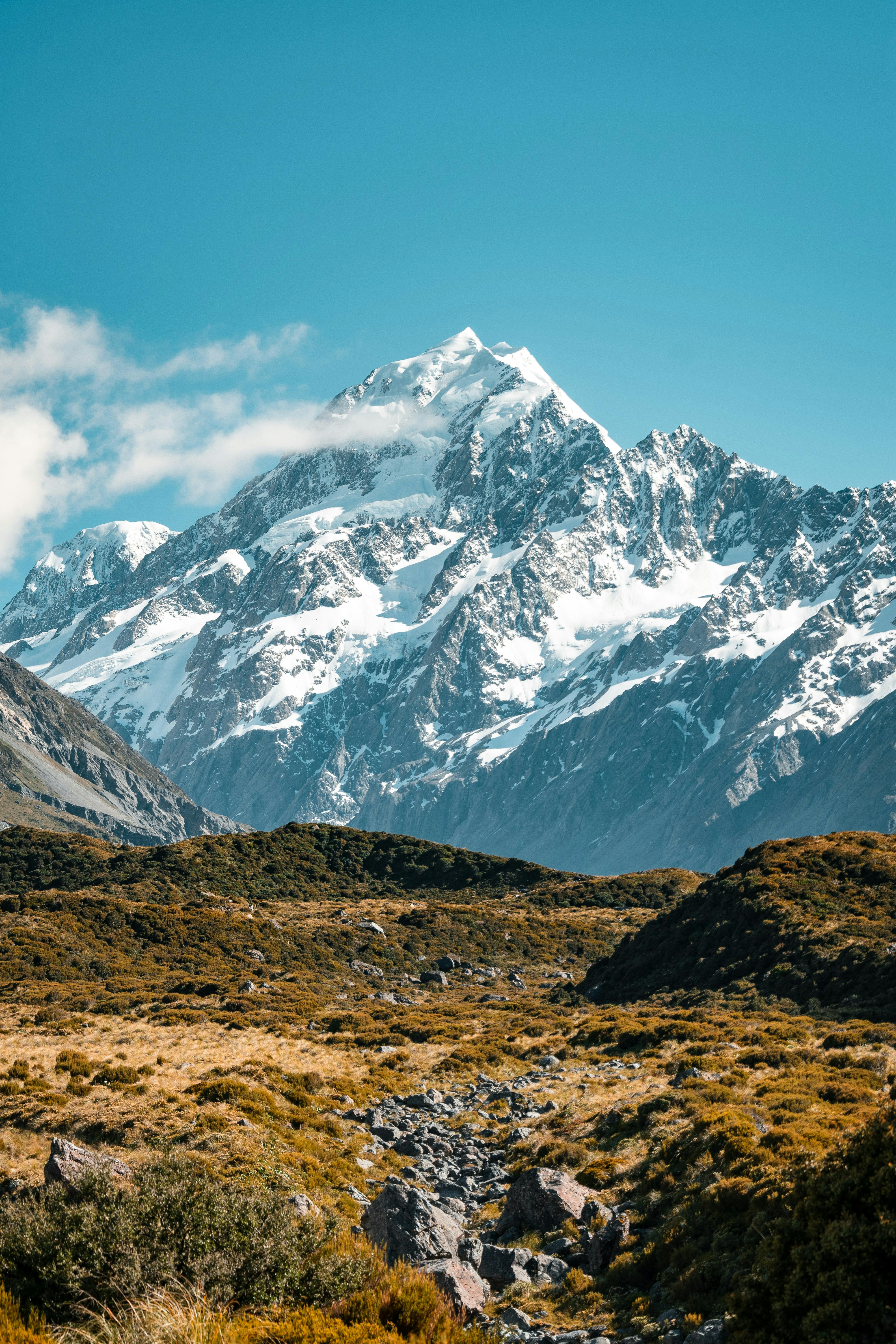 A rocky hillside lays in the foreground with Mount Cook towering in the distance. 