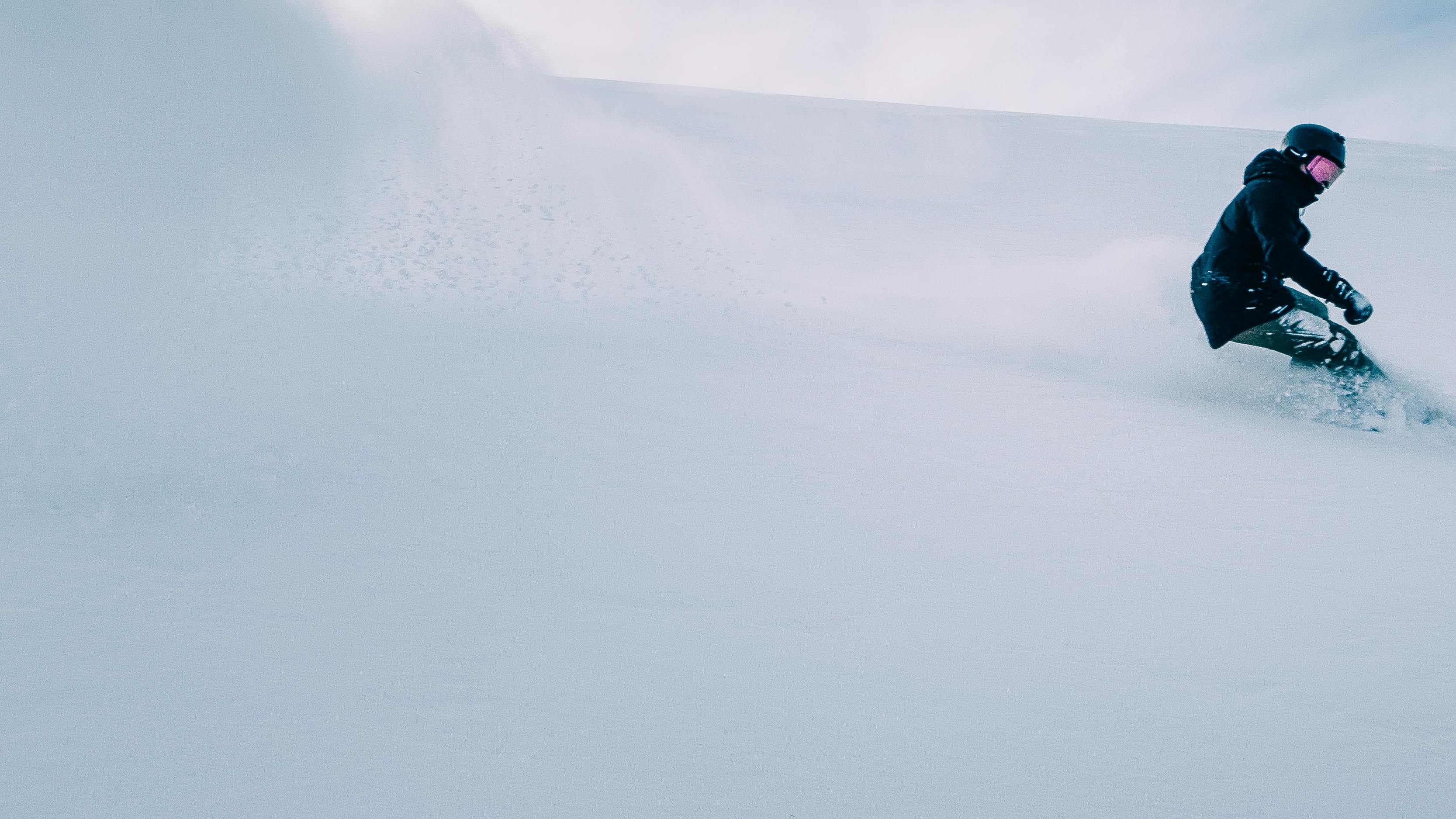 A snowboarder turns down a snowy hill. 