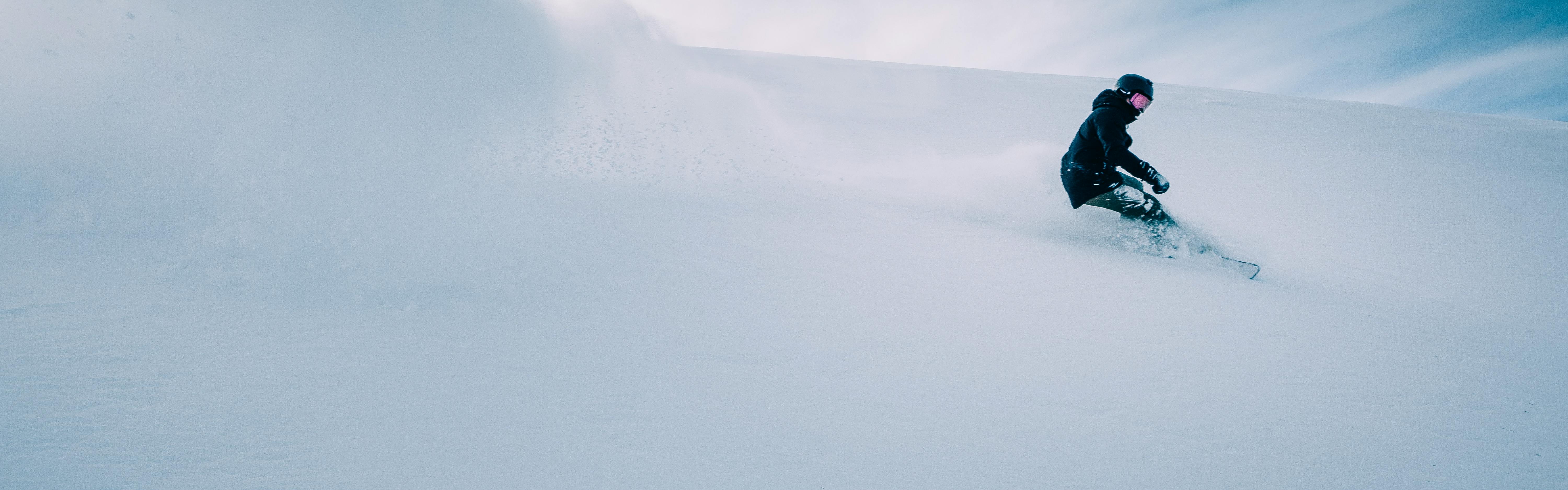 A snowboarder turns down a snowy hill. 