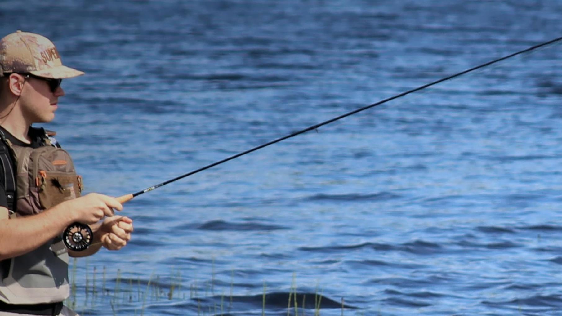 A man standing in a body of water casting a fly rod.