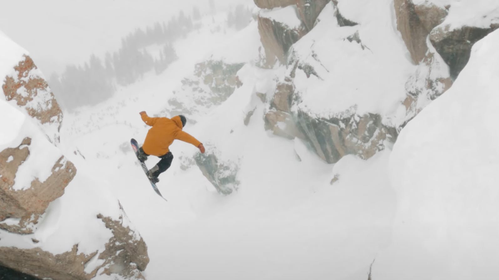 A snowboarder drops into Corbet's couloir. He is wearing an orange jacket.