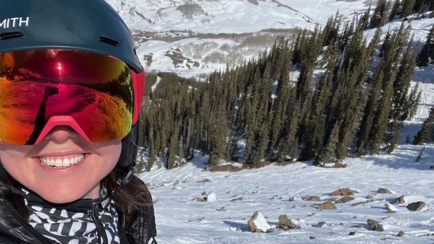 A woman at the top of a ski run smiling and wearing the Smith I/O MAG XL Goggles.