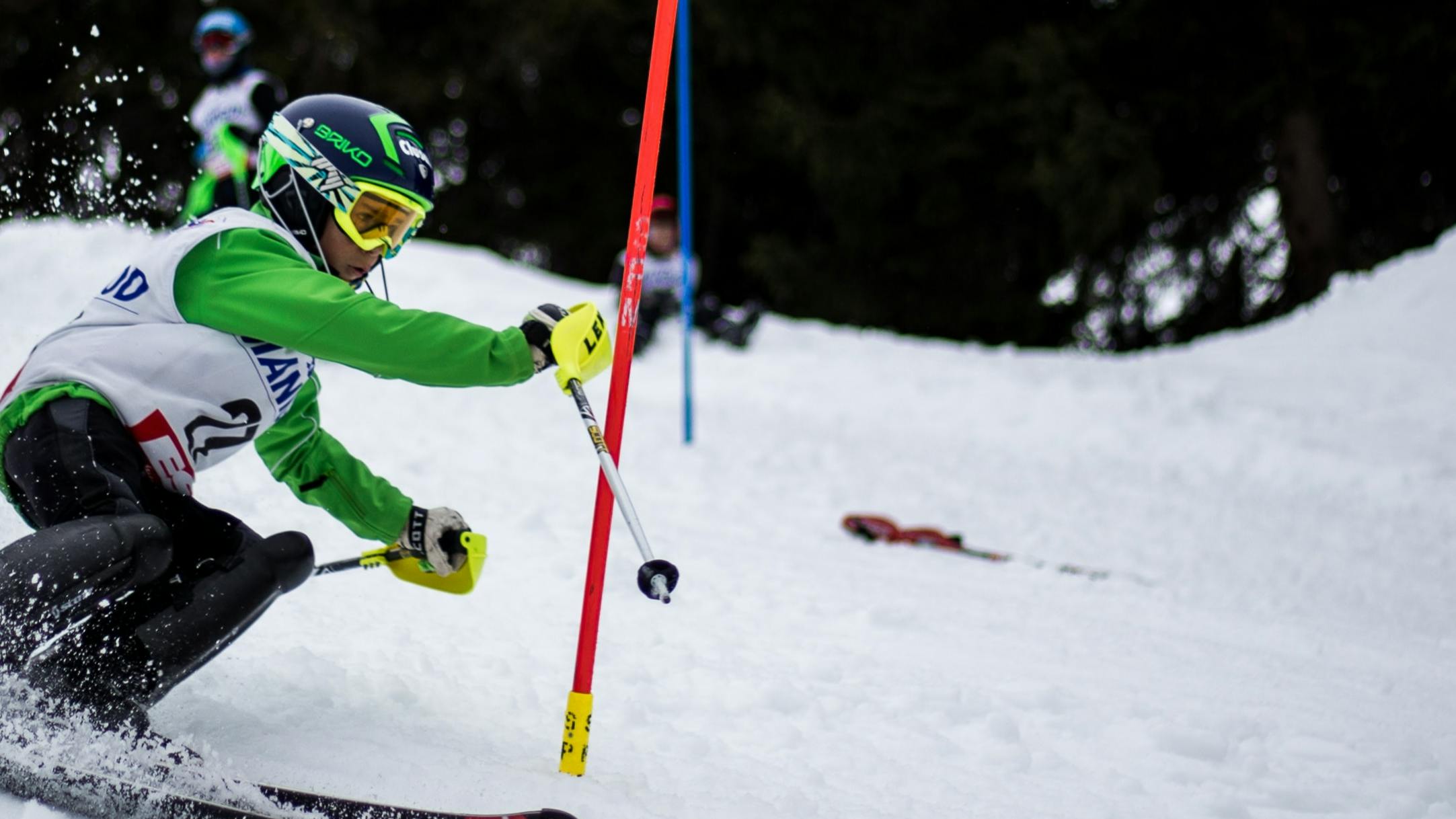 Someone in a green shirt and white jersey ski races downhill. 