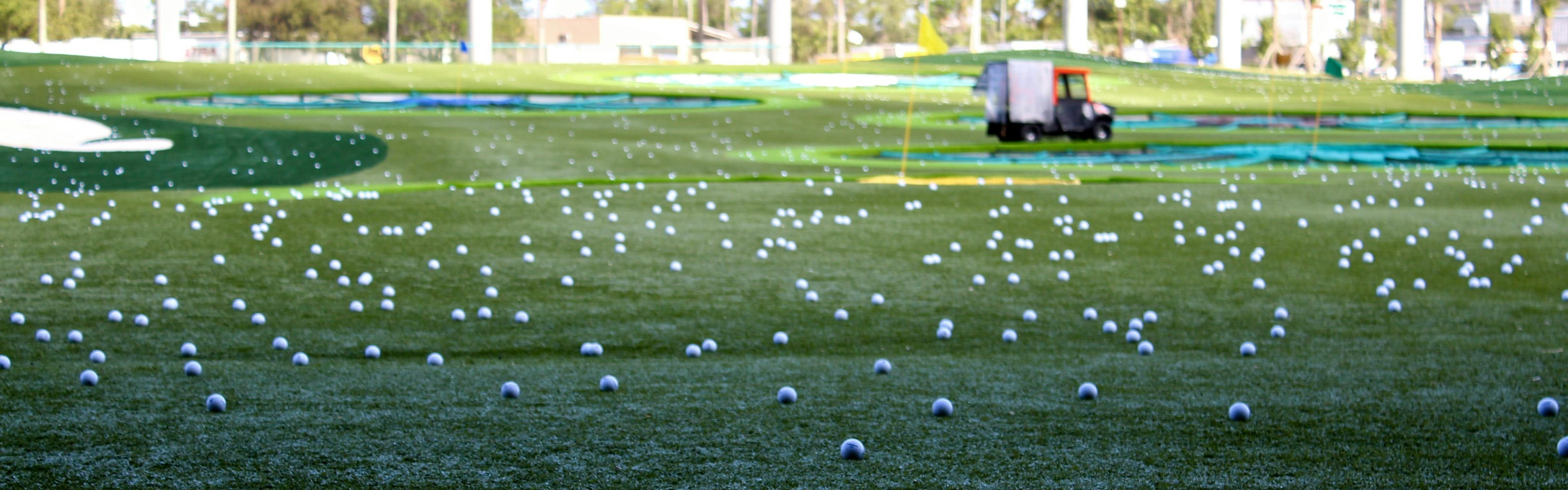 A bunch of golf balls on a driving range.