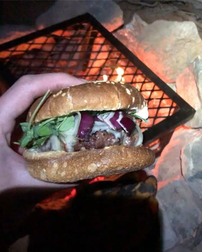 An image of the author's burger made on a grill grate over a campfire. There's lettuce, red onion, and cheese on it.