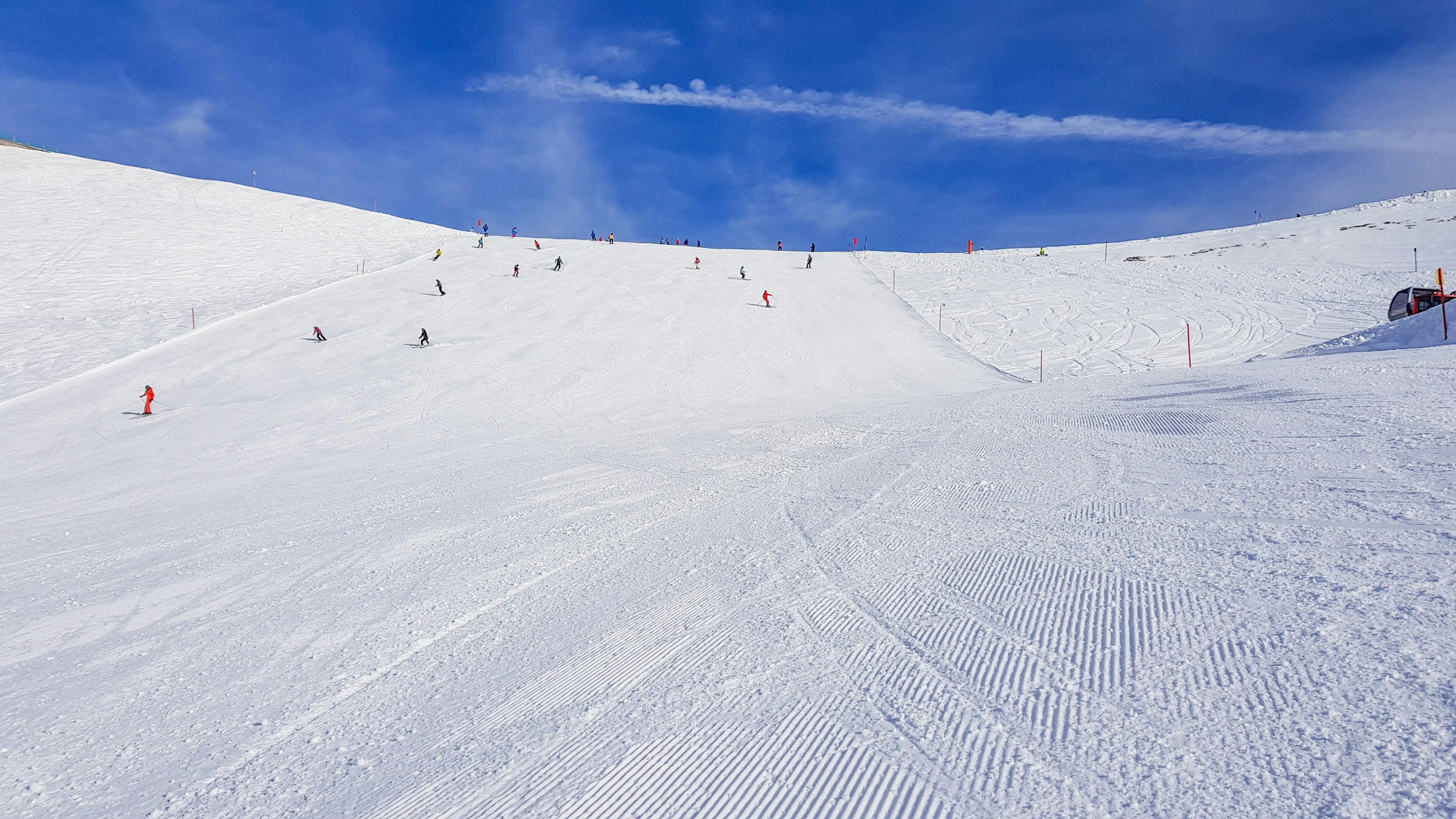 A wide-open groomed run at a ski hill with numerous skiers on it